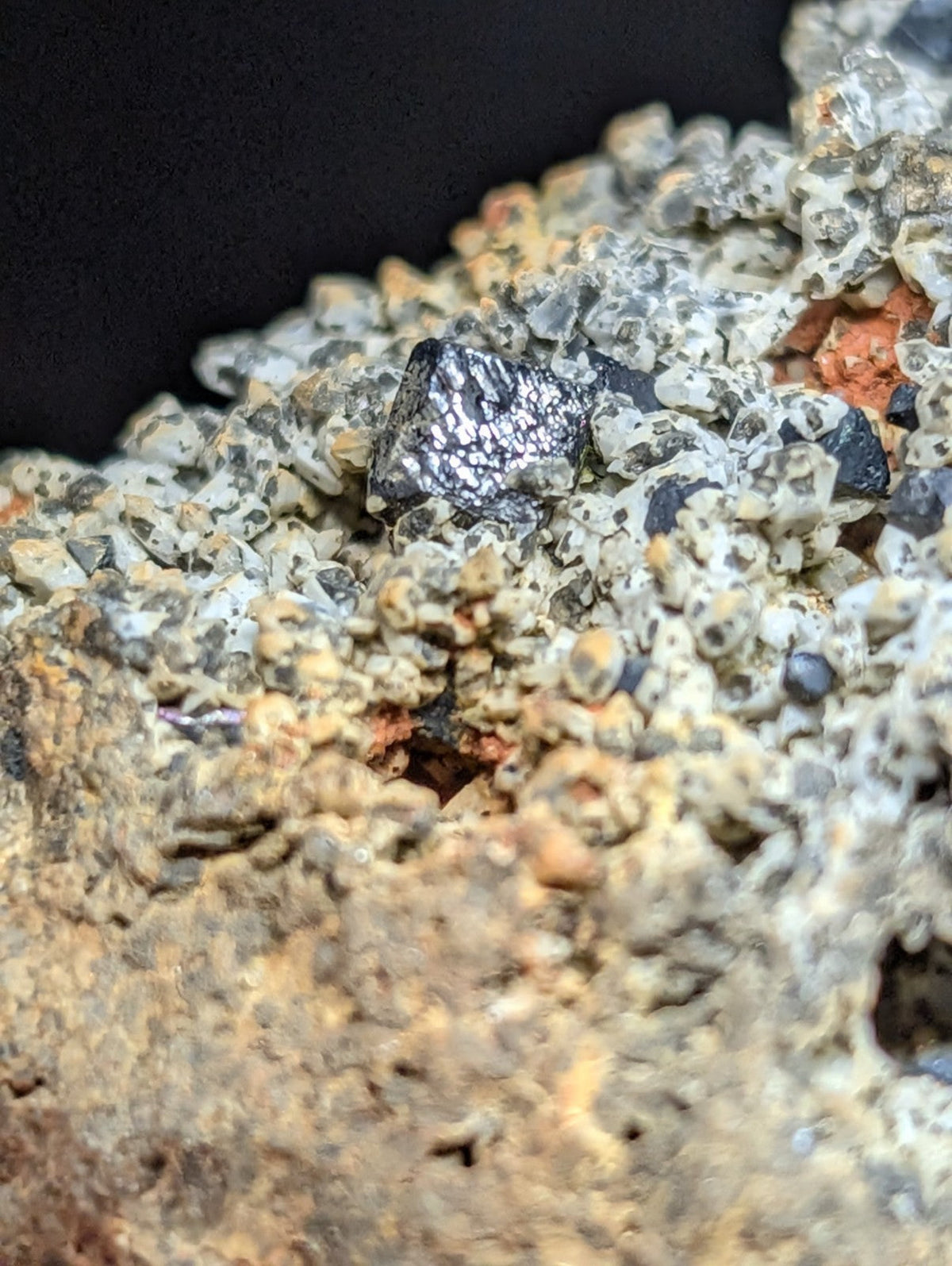 A dark, metallic-looking mineral specimen with a rough, crystalline surface embedded in a matrix of lighter-colored rock.