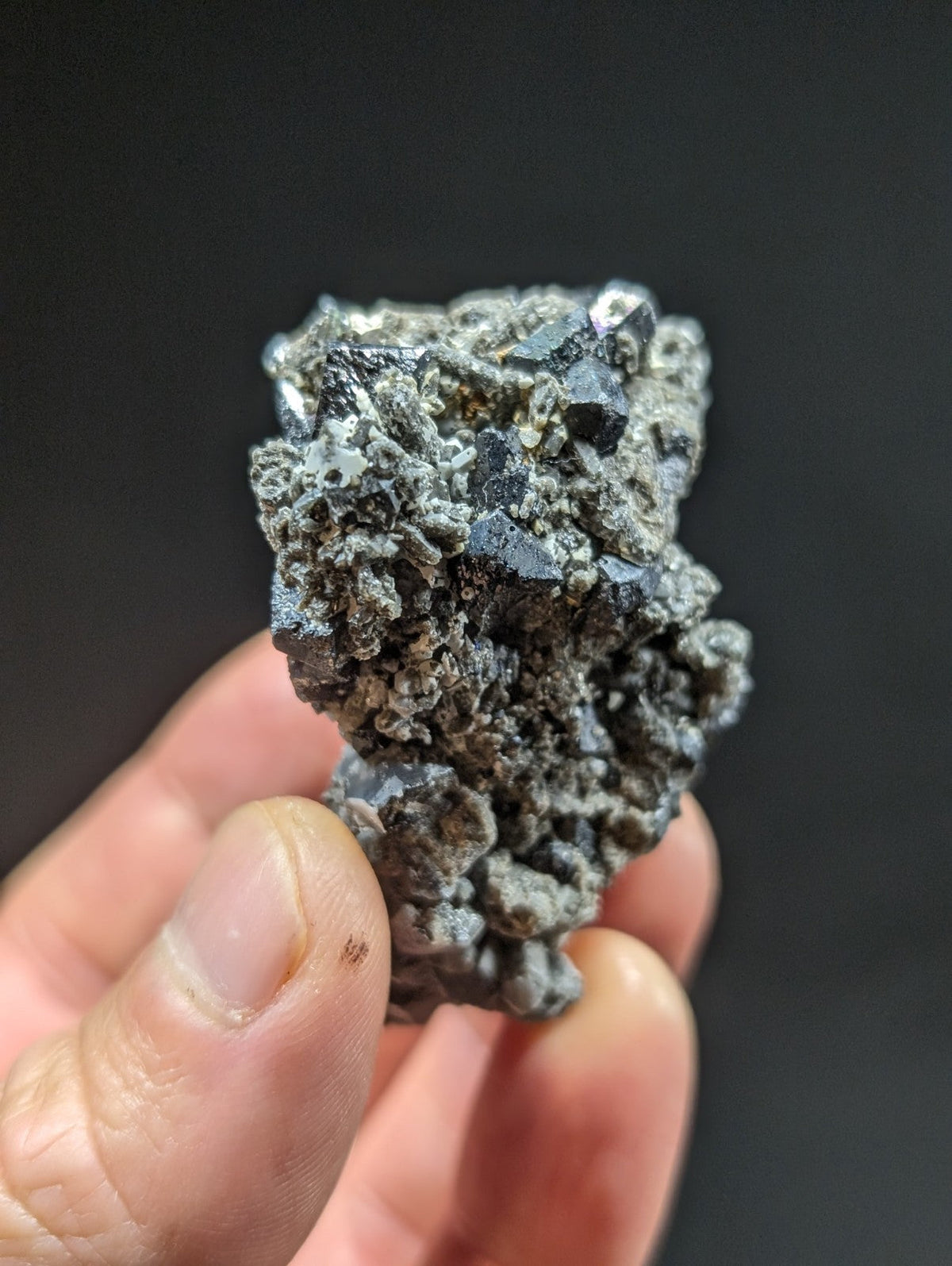 A rough, irregularly shaped mineral specimen with a mix of dark gray and metallic silver crystals embedded in a lighter gray matrix.