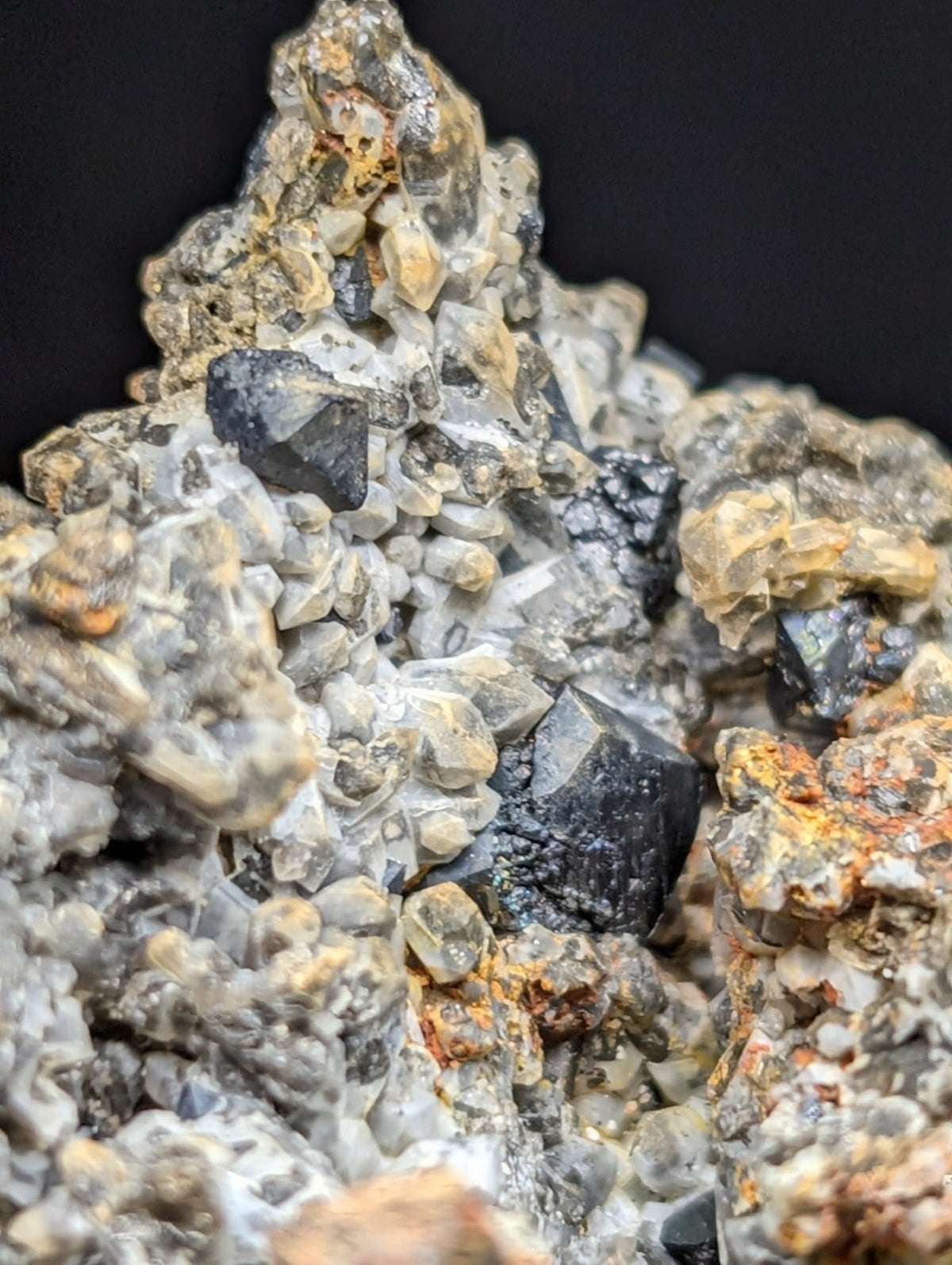 A striking mineral specimen featuring a cluster of translucent gray crystals interspersed with dark, metallic-looking black minerals and patches of rusty orange oxidation.