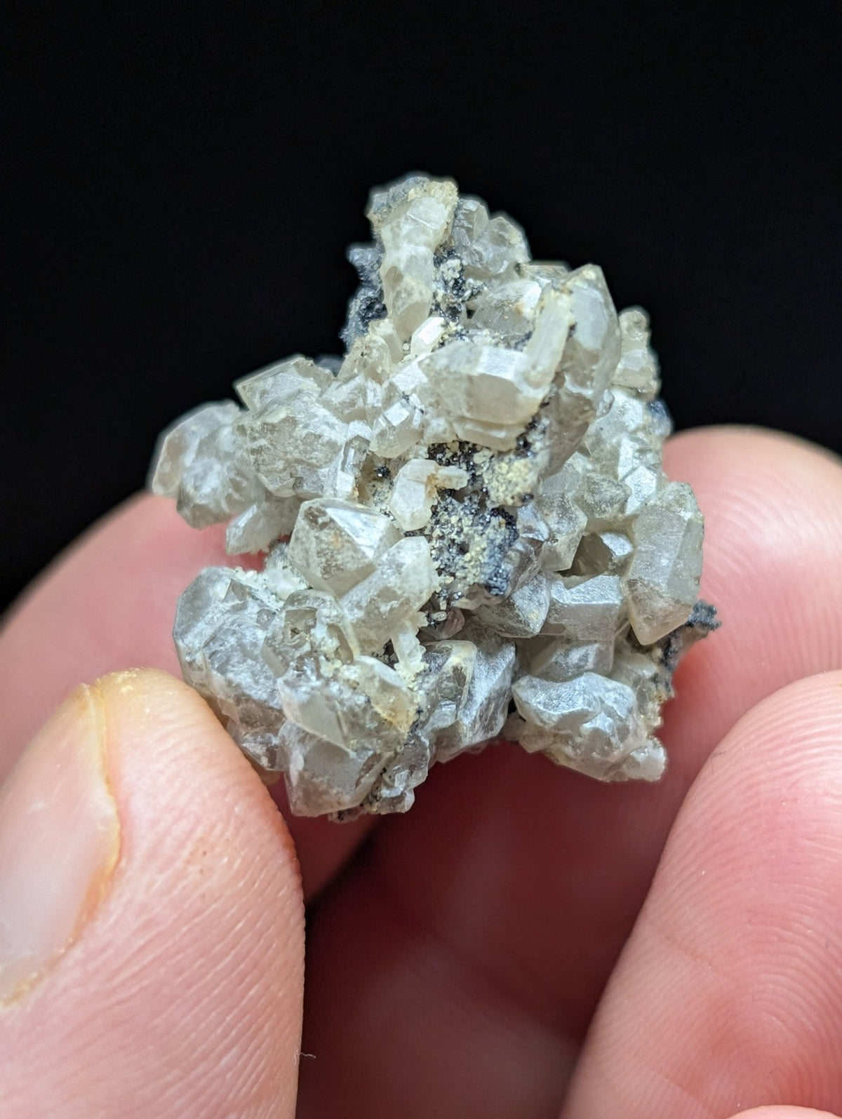 A cluster of translucent, pale gray crystals with sharp facets and some darker mineral inclusions.