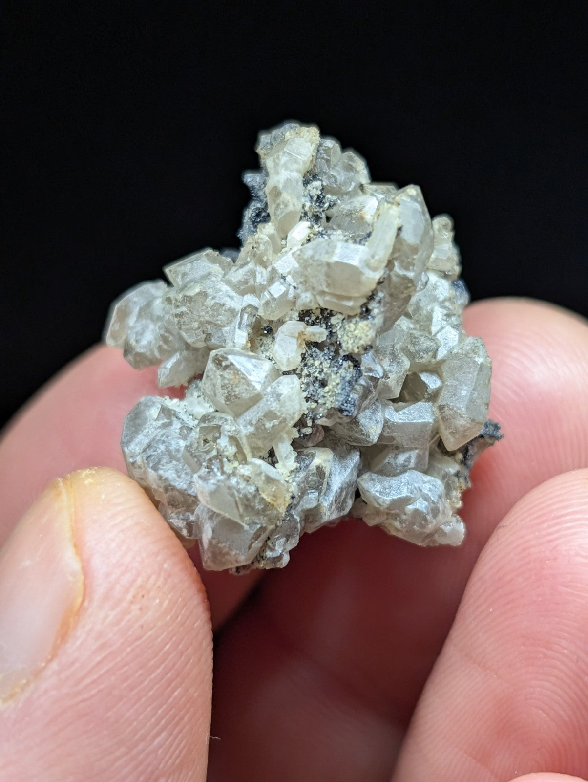A cluster of translucent, pale gray crystals with sharp facets and some darker mineral inclusions.