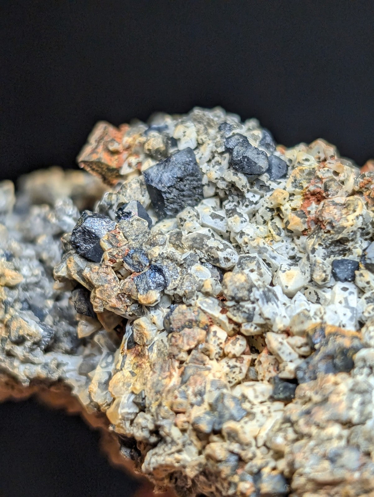 A rugged mineral specimen featuring dark, angular crystals embedded in a matrix of speckled gray and orange rock.