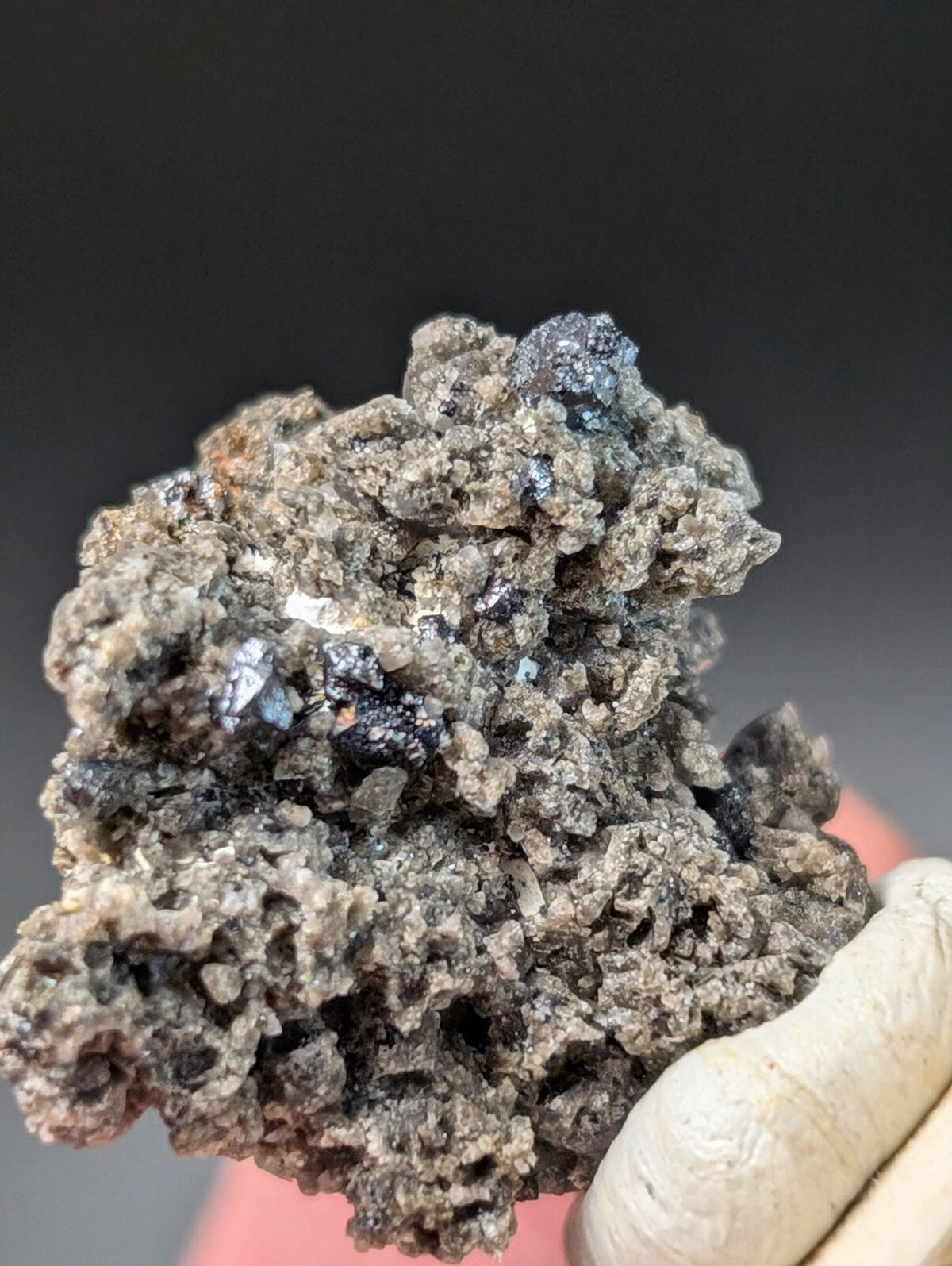 A rugged, dark gray mineral specimen with embedded black and blue crystalline inclusions.