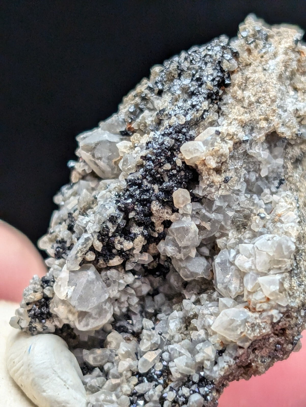 A rugged, naturally formed mineral specimen featuring translucent gray crystals interspersed with dark black specks and earthy brown matrix.