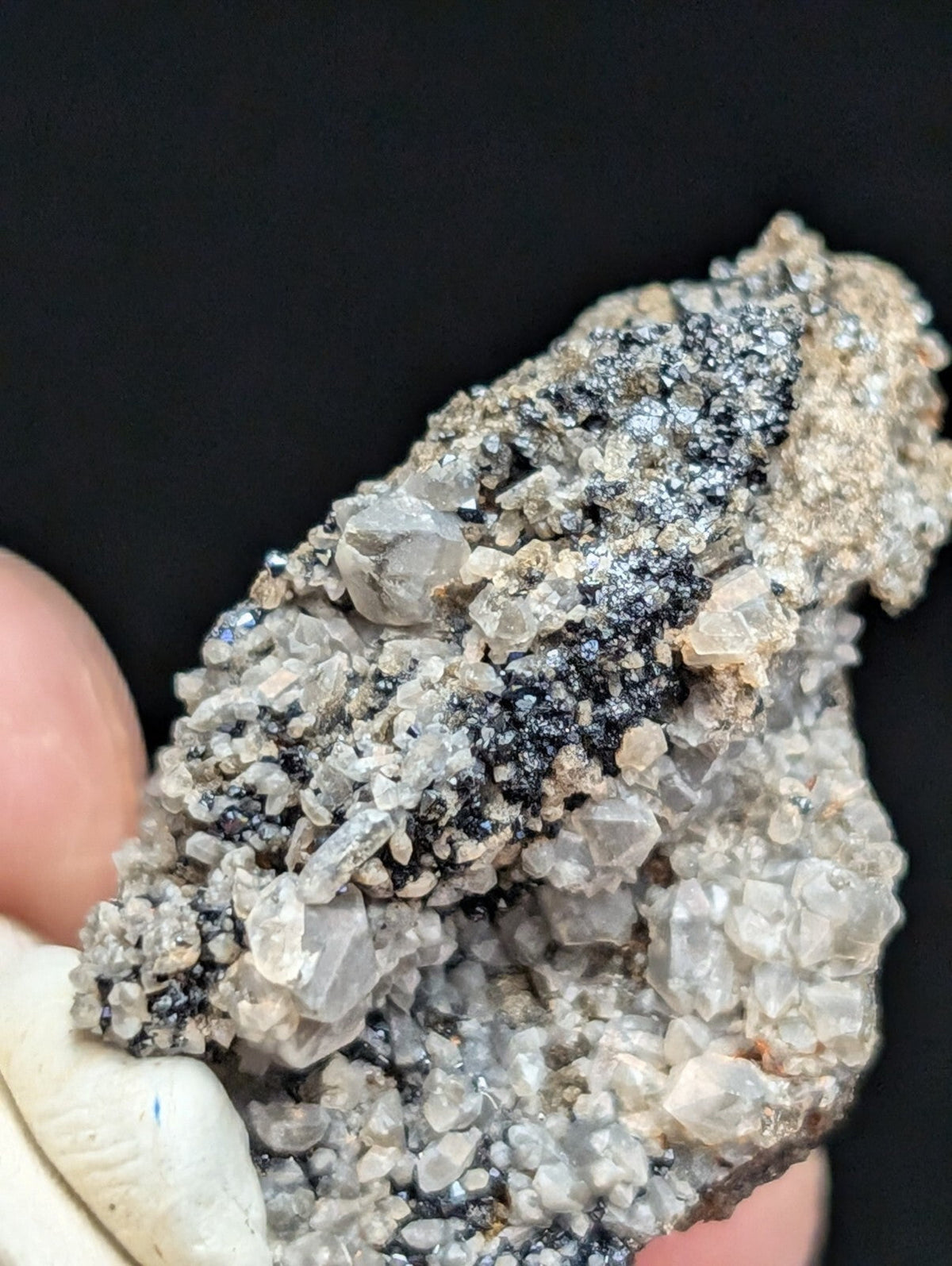 A rugged, naturally occurring mineral specimen featuring translucent gray crystals interspersed with dark metallic inclusions and a rough, earthy matrix.