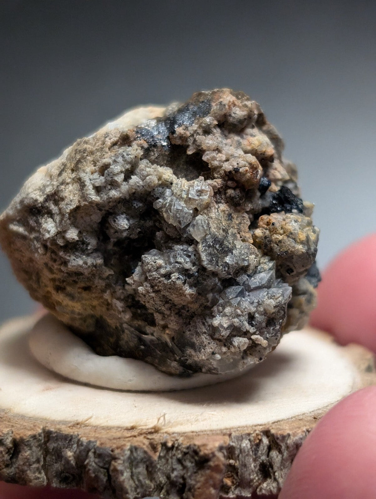 A rugged, earthy-toned mineral specimen with a rough, textured surface featuring patches of dark gray and translucent crystalline formations.