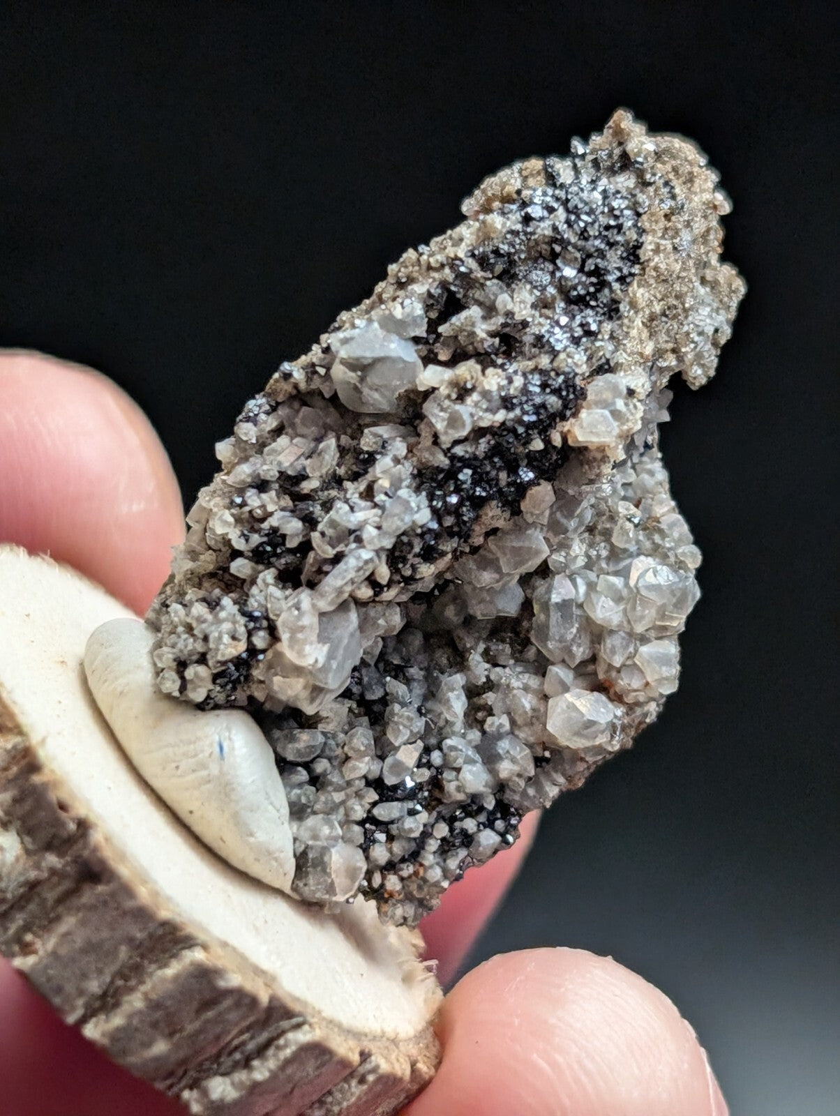 A gray and black crystalline mineral specimen with translucent, faceted crystals growing from a rough, earthy matrix.