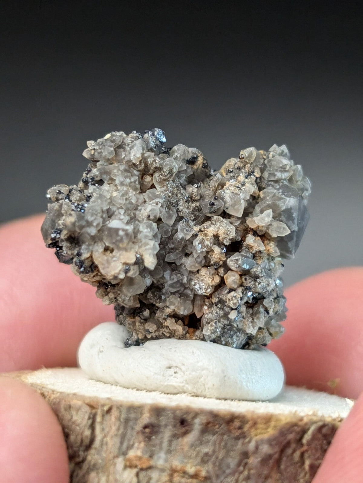 A cluster of translucent gray crystals with specks of black and blue, set atop a white ceramic base.