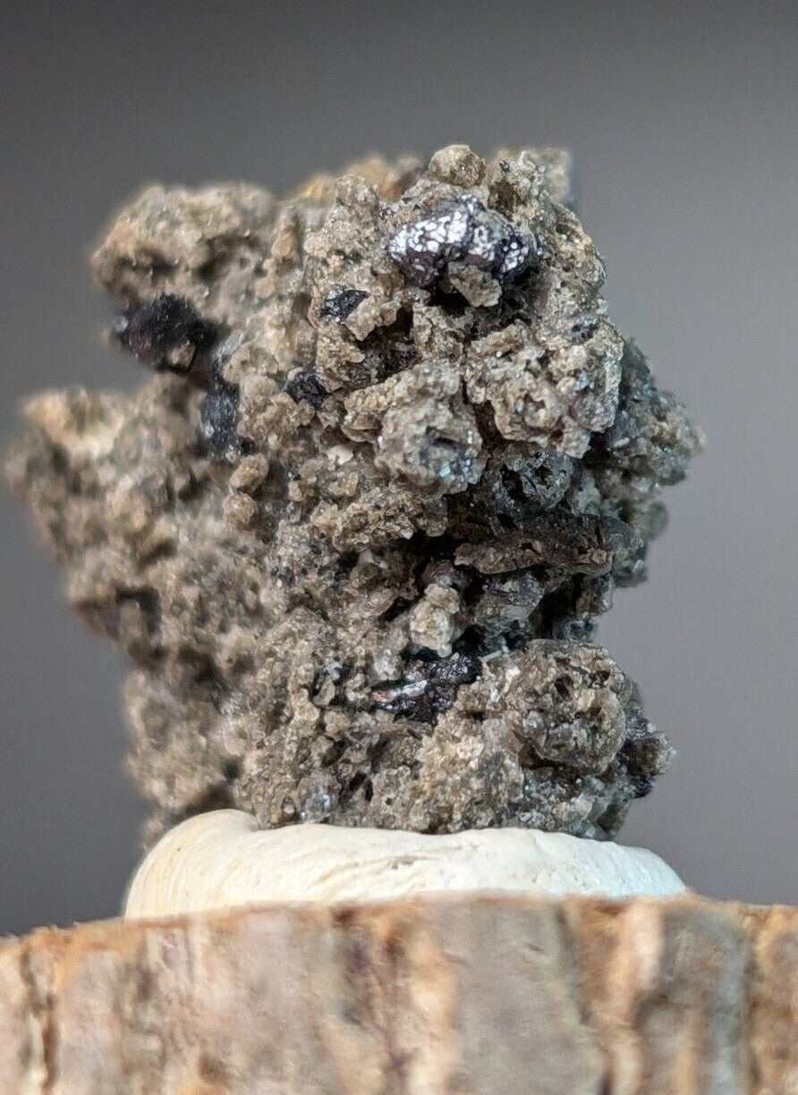 A rugged, grayish mineral specimen with dark metallic inclusions and a rough, textured surface.