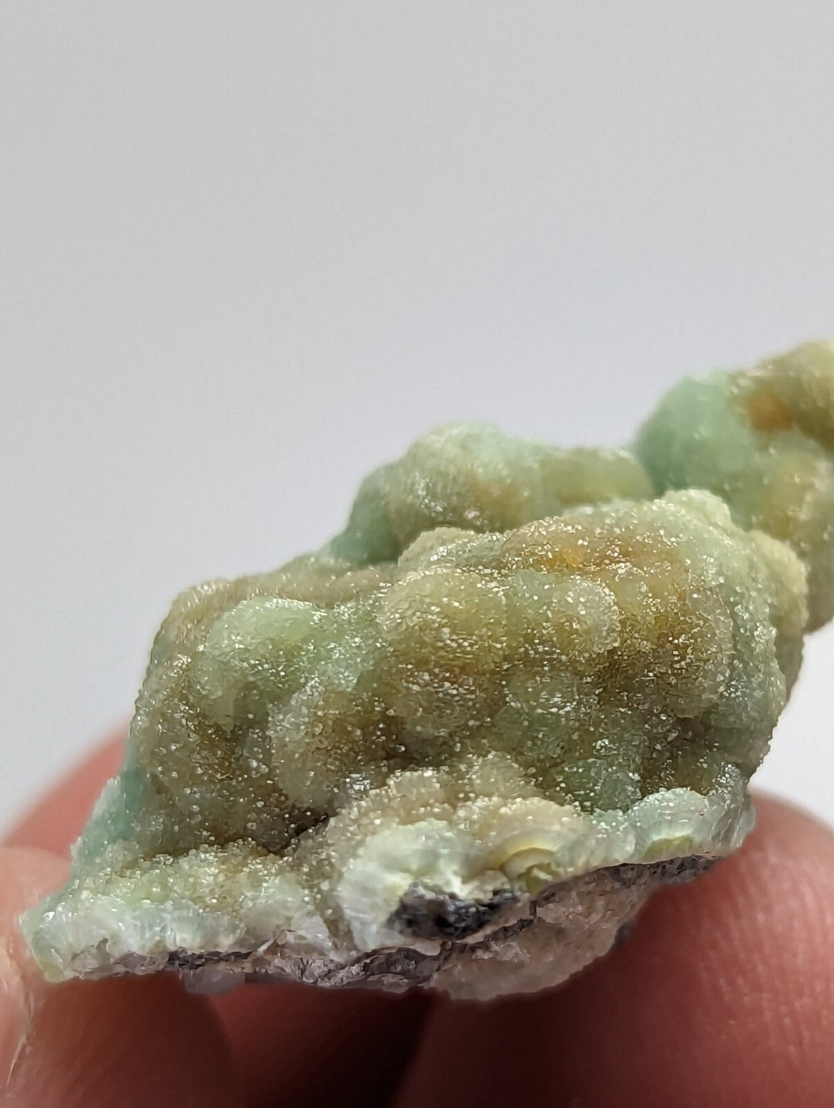 A textured, light green and yellowish mineral specimen with a crystalline surface held between fingers.