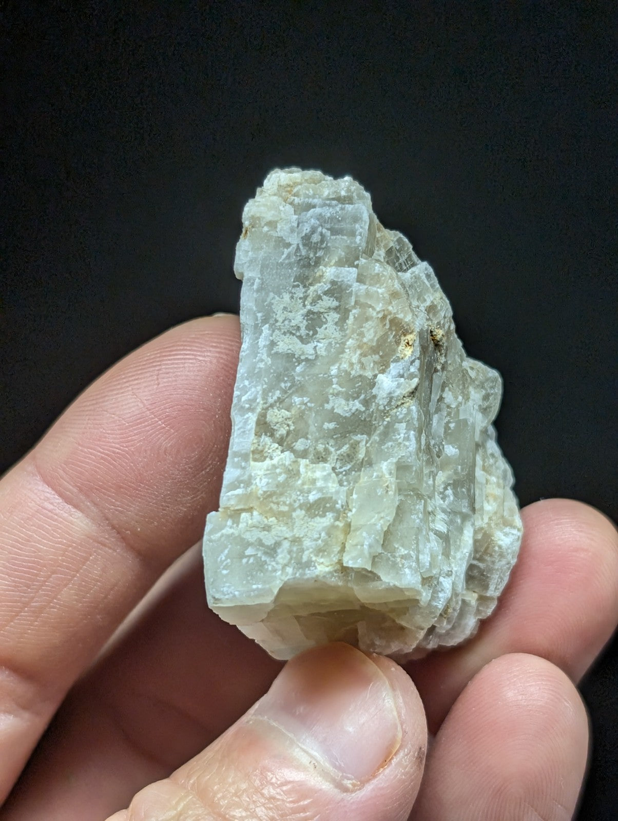 A translucent, pale greenish-white mineral specimen with a rough, crystalline texture and visible layered growth patterns.