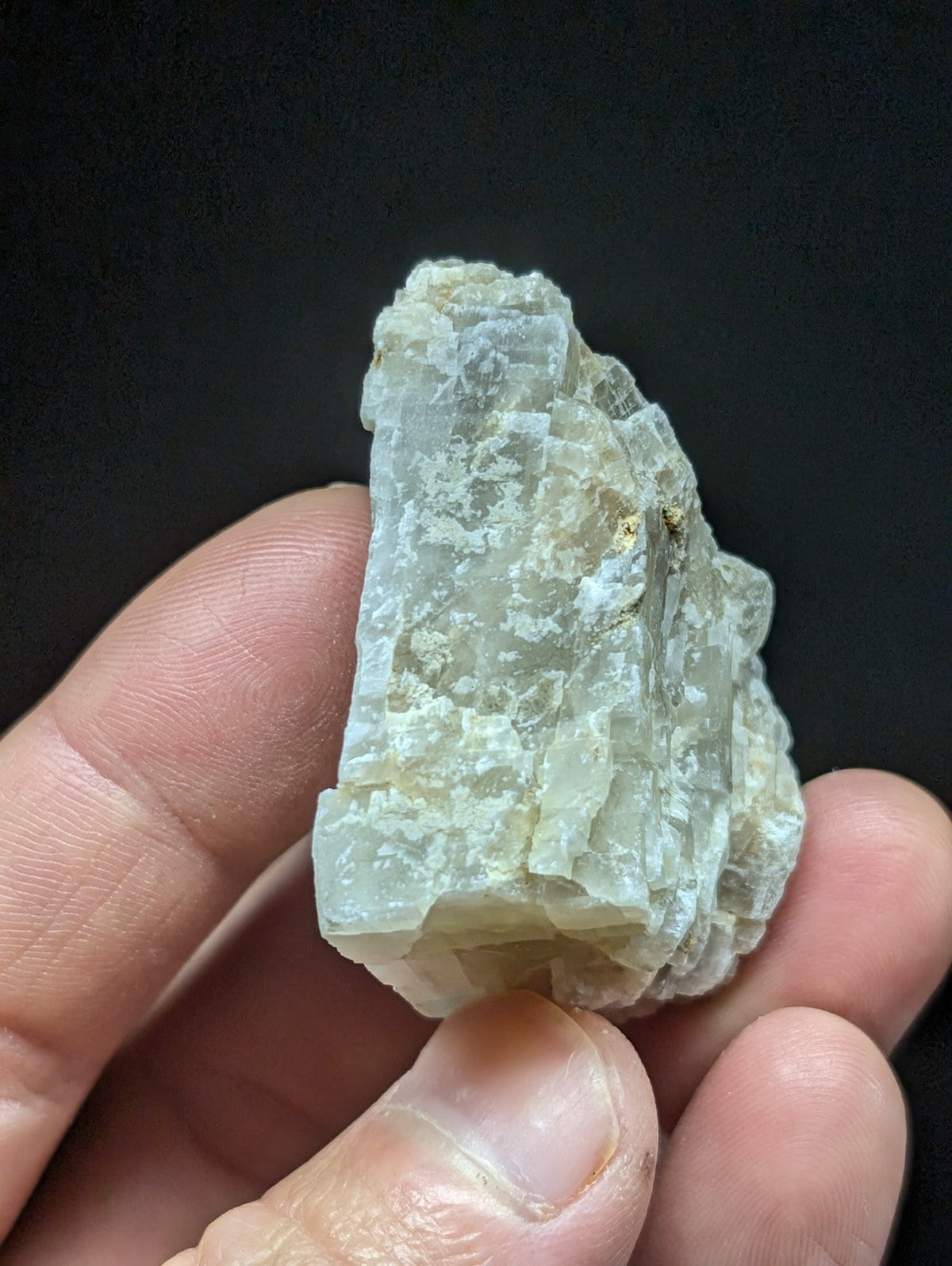 A translucent, pale greenish-white mineral specimen with a rough, crystalline texture and visible layered growth patterns.