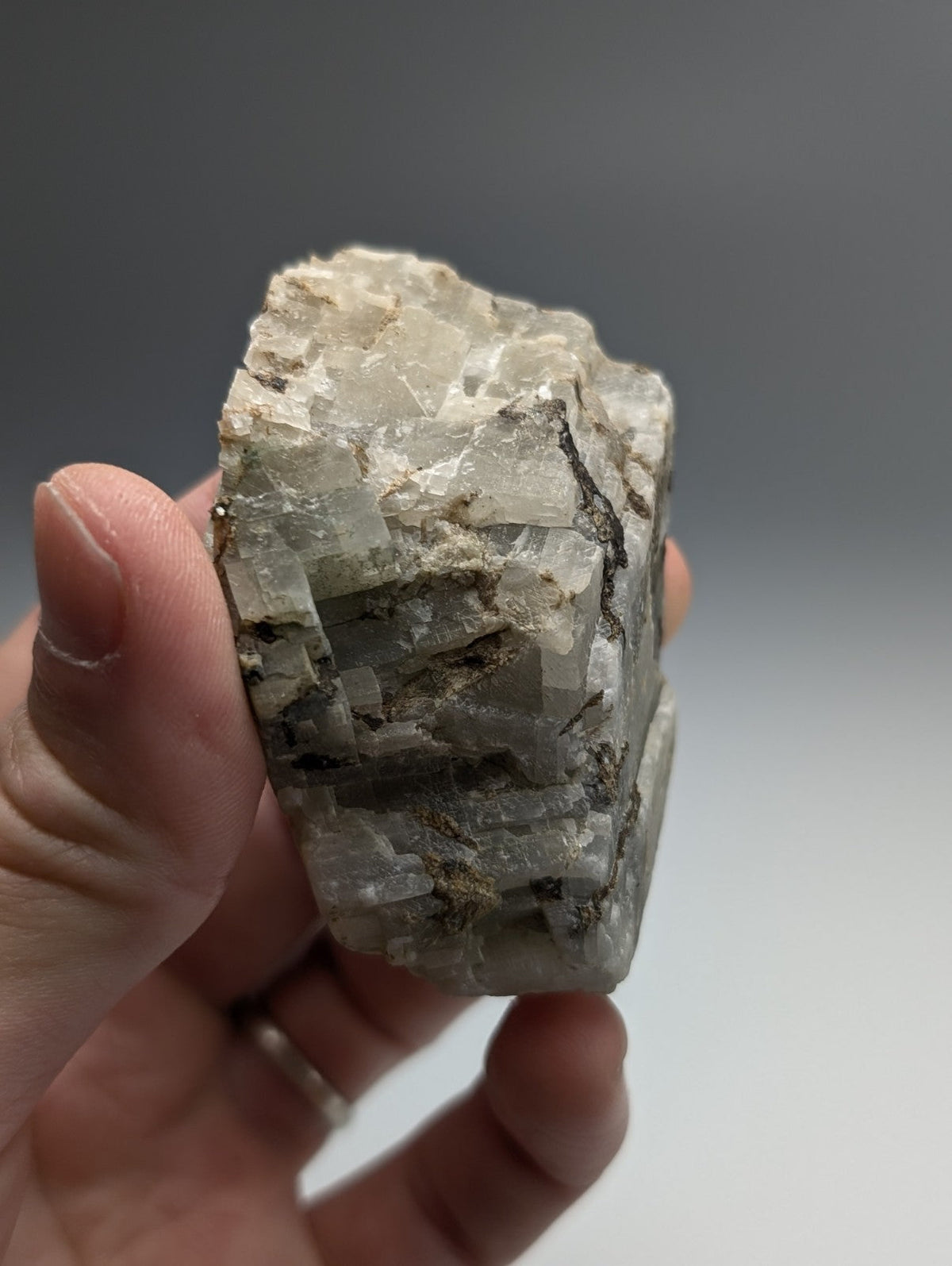 A hand holds a rough translucent white calcio carbonatite mineral with crystalline facets and dark veining from Arkansas