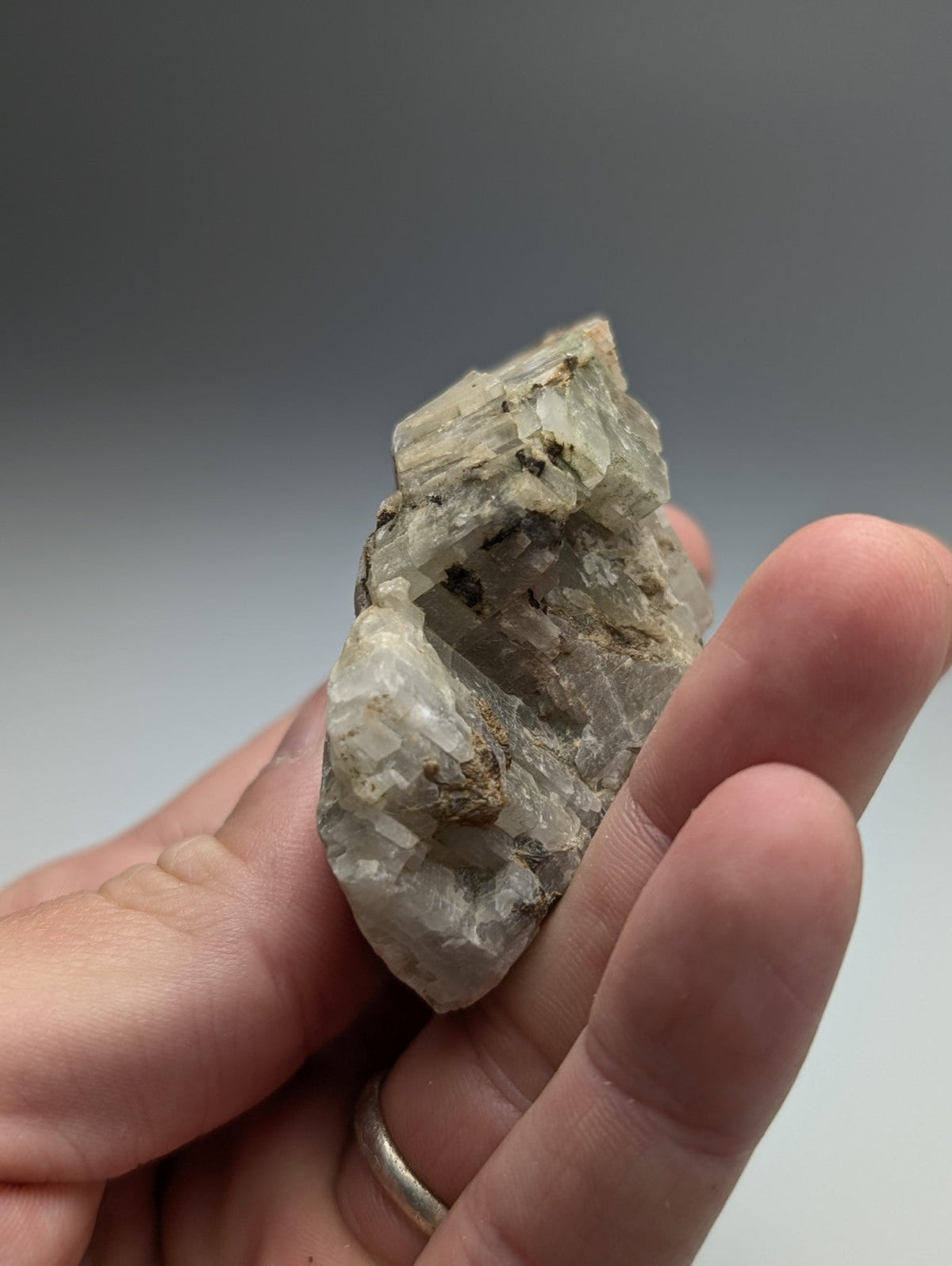 A translucent pale greenish-white calcio carbonatite mineral with crystalline facets and dark inclusions from Arkansas