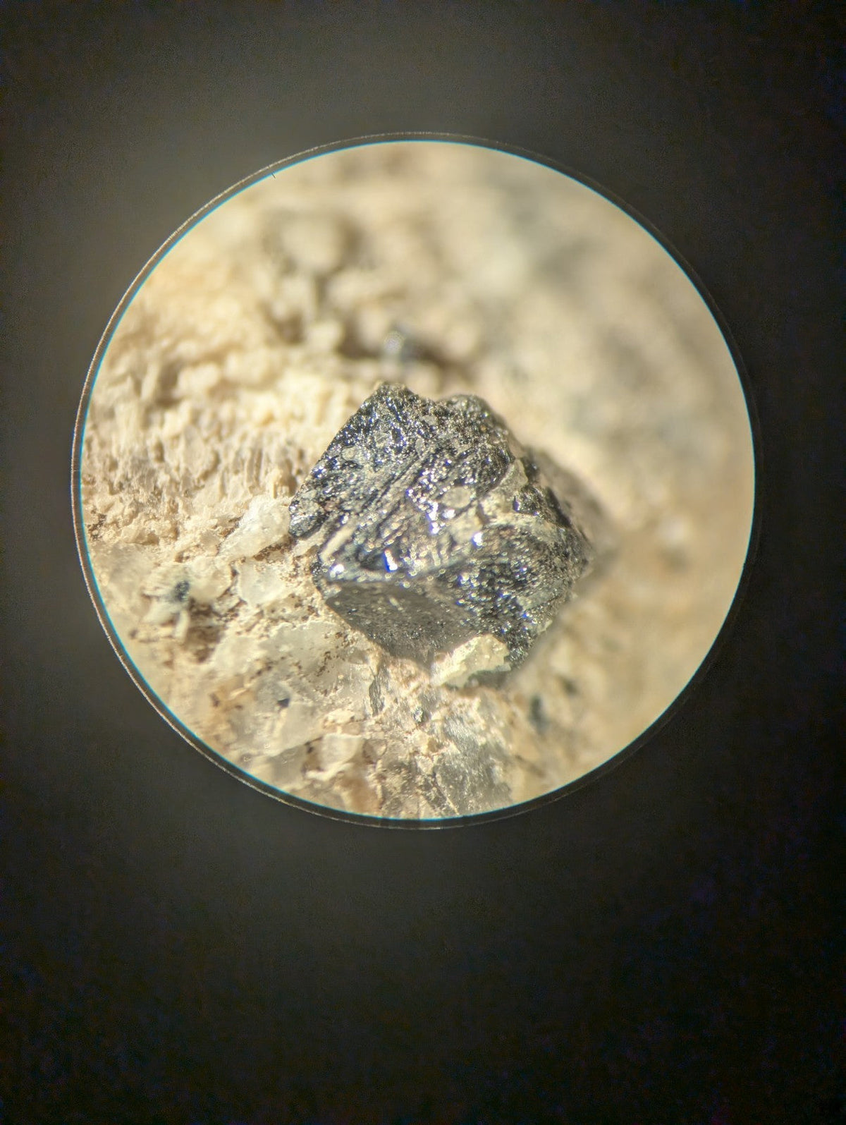 A dark, metallic mineral specimen with a rough, faceted surface and subtle iridescent highlights.