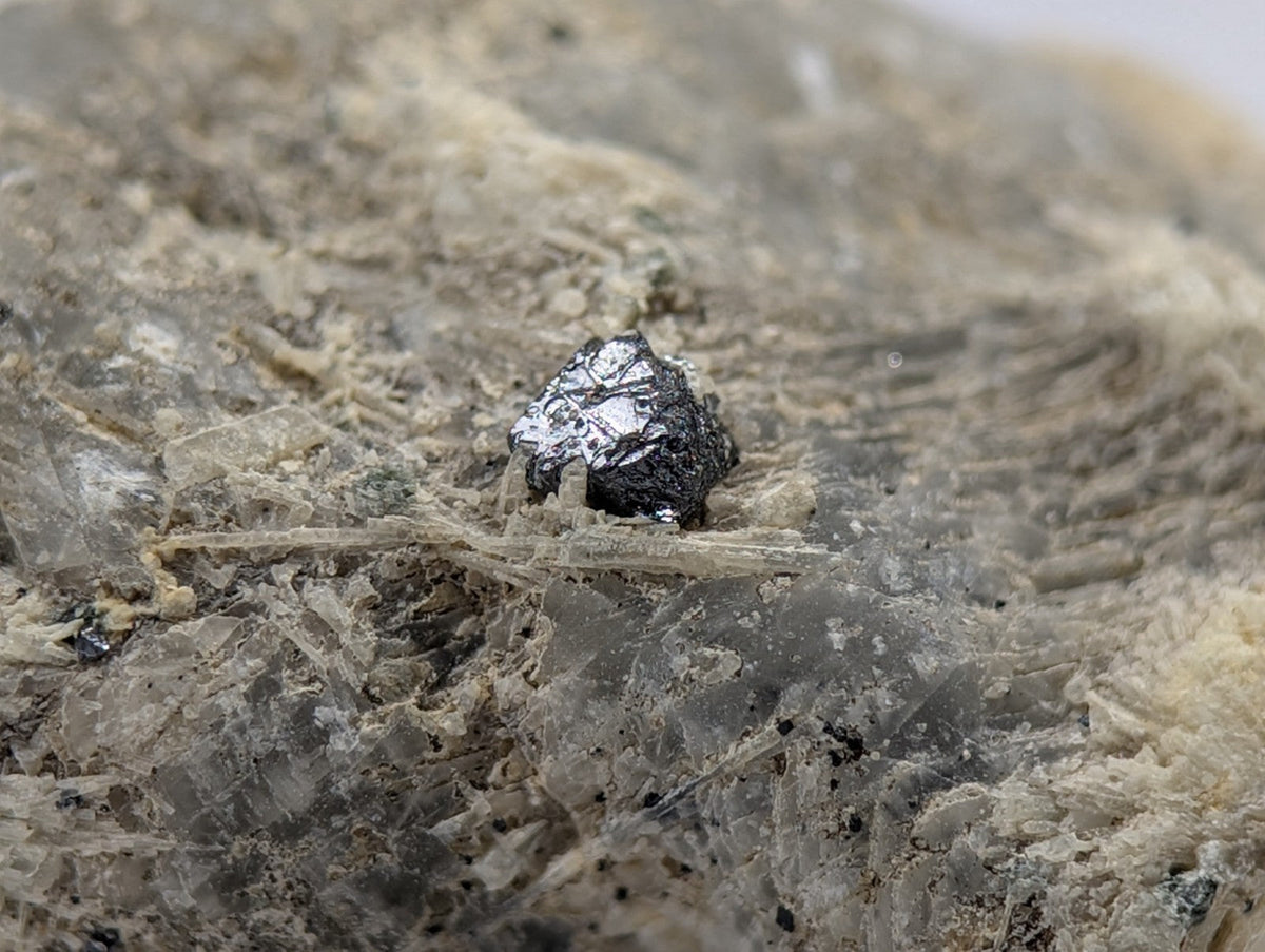 A dark, metallic mineral specimen with a rough, irregular surface sits embedded in a matrix of translucent quartz and earthy tones.