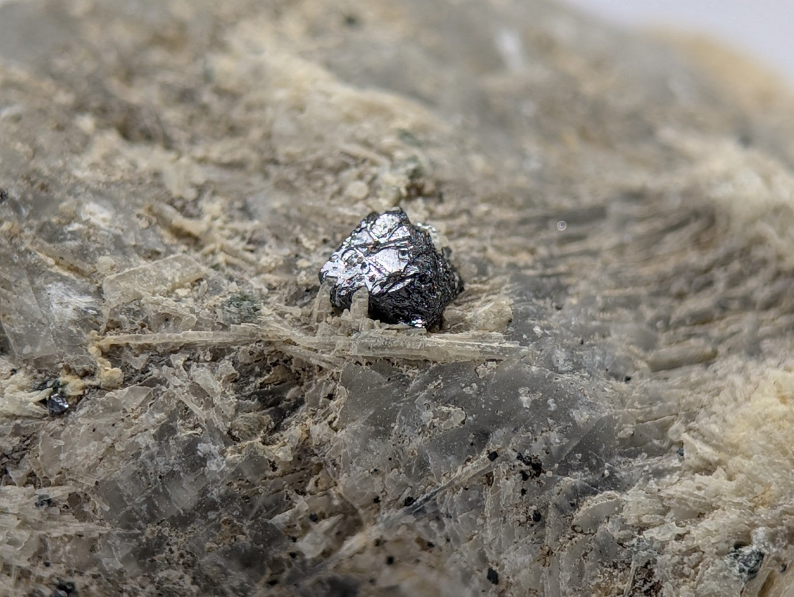 A dark, metallic mineral specimen with a rough, irregular surface sits embedded in a matrix of translucent quartz and earthy tones.
