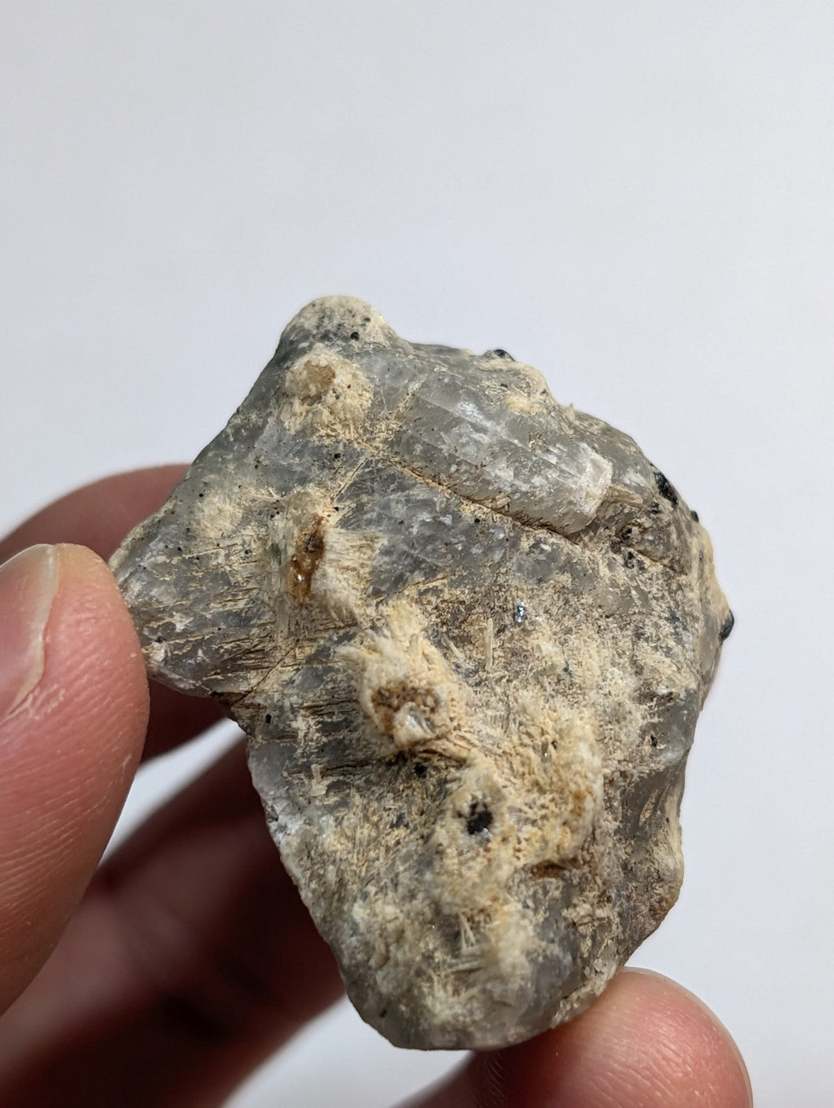 A rough, grayish mineral specimen with visible crystalline facets and patches of lighter, fibrous material.