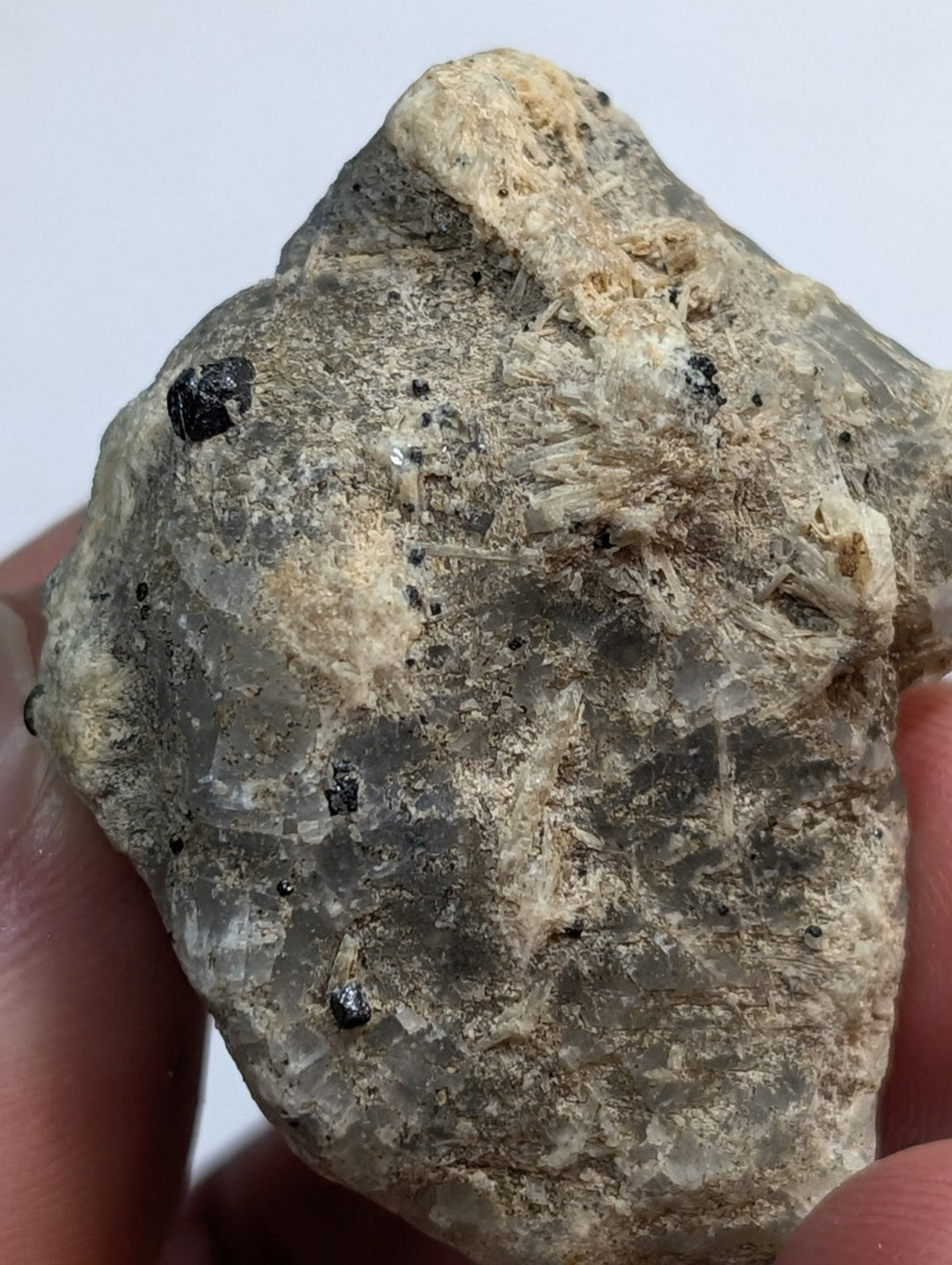 A rough, grayish-green mineral specimen with translucent crystalline formations and scattered dark inclusions.