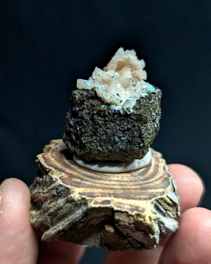 A dark, rough-textured mineral specimen topped with a cluster of translucent, crystalline formations in pale pink and blue hues.