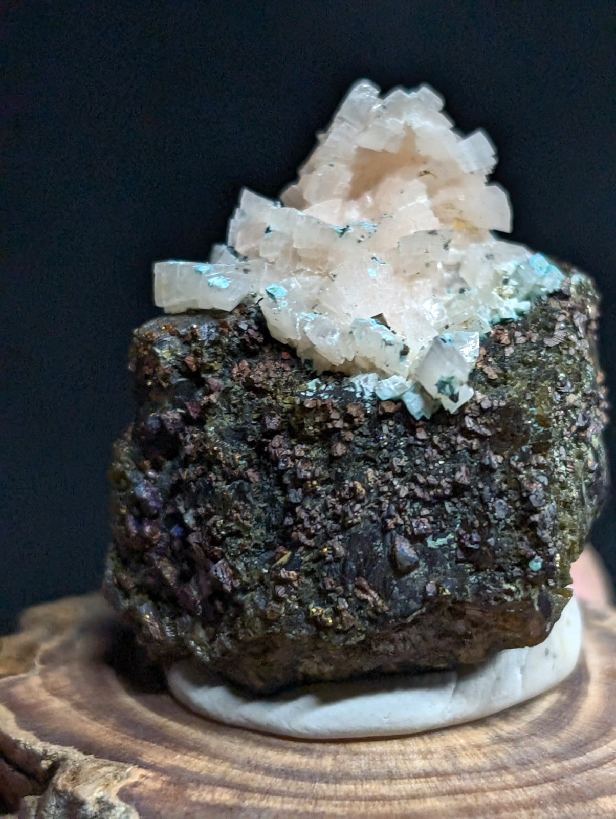 A striking mineral specimen featuring a cluster of translucent, pale pink crystals atop a dark, textured matrix with hints of green and purple.