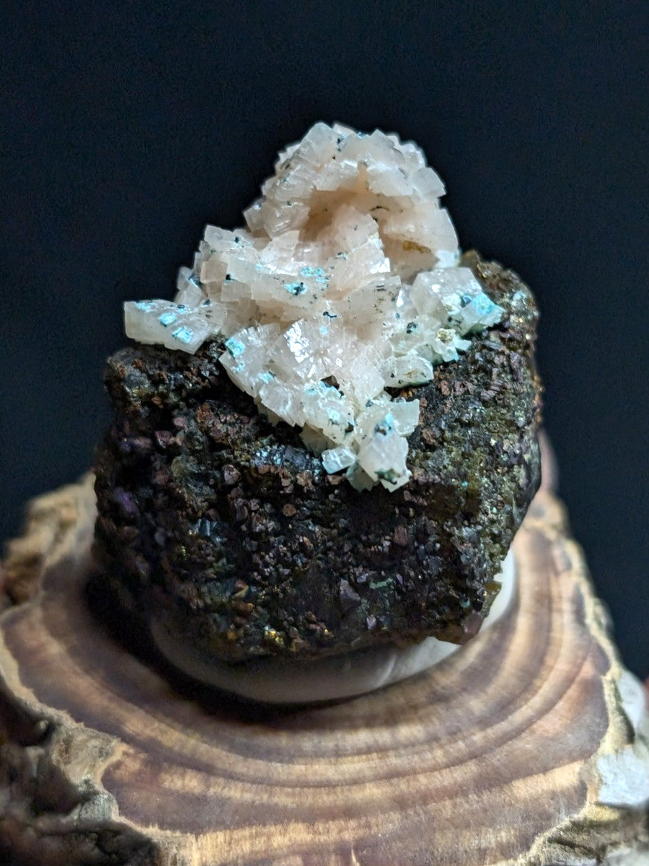 A cluster of translucent, crystalline minerals with a pale pinkish hue and subtle blue flecks rests atop a dark, rough-textured rock base.