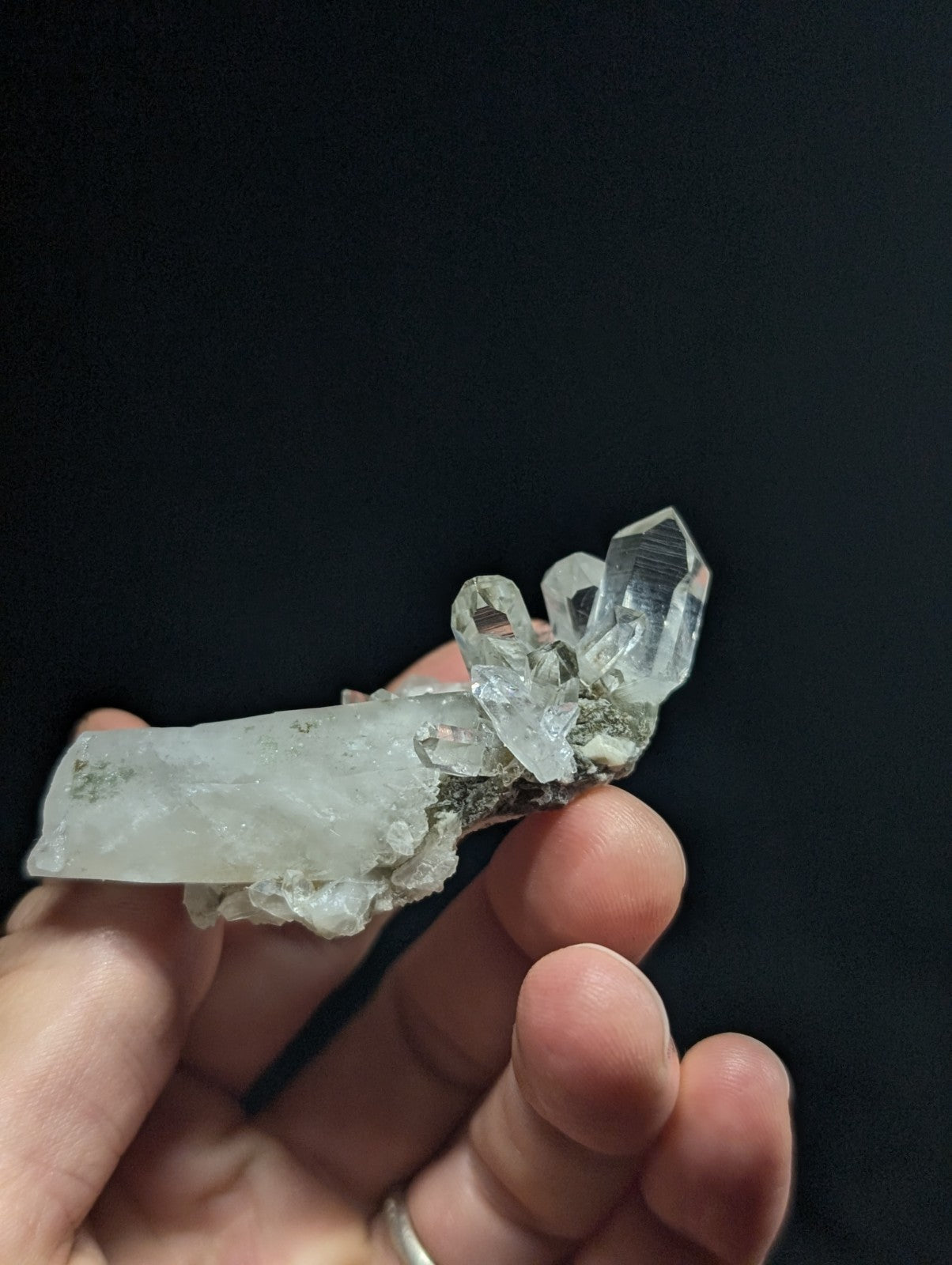 A translucent, clear quartz crystal cluster with a rough, earthy base and sharp, faceted points.