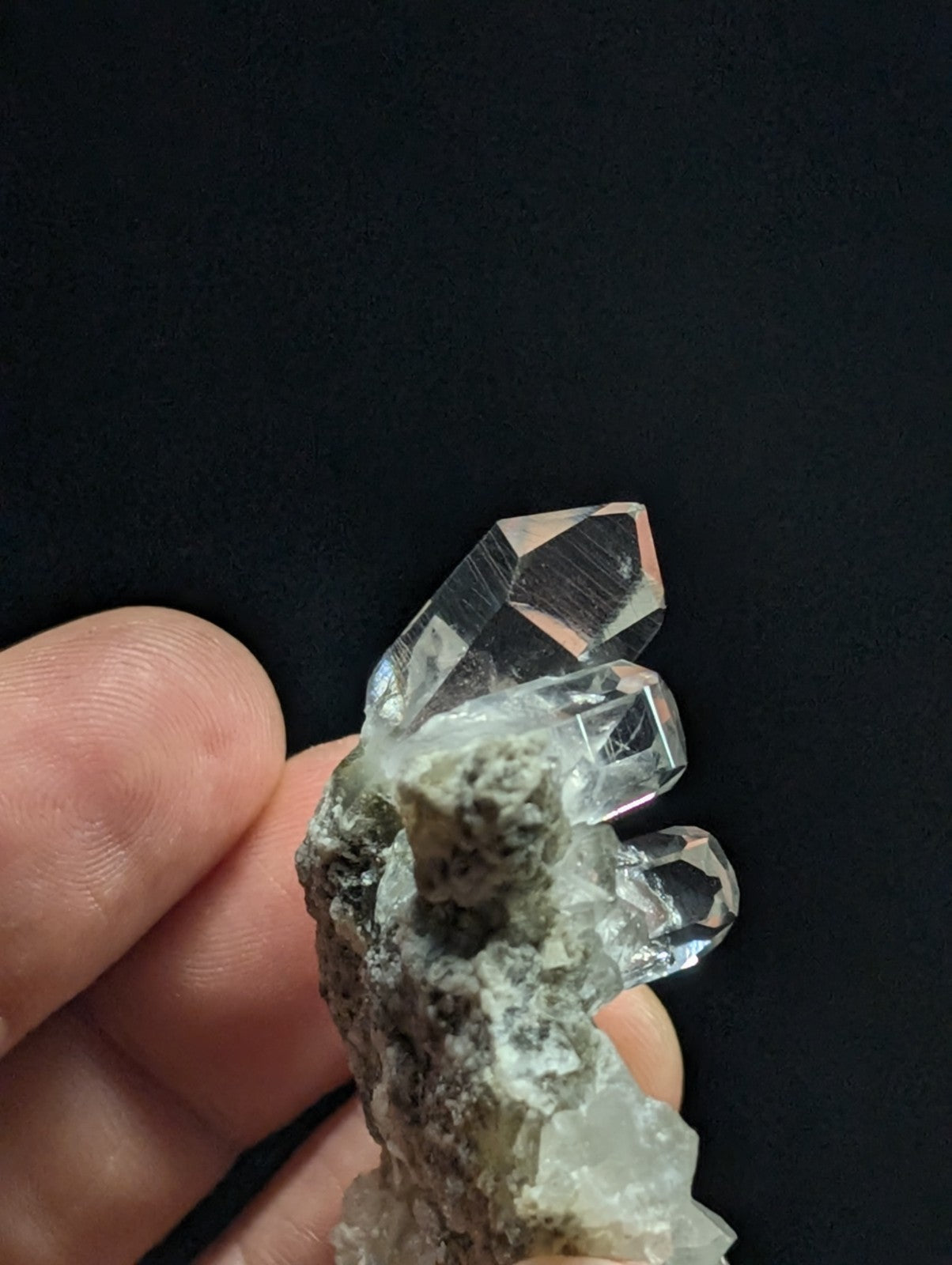 A clear quartz crystal cluster with sharp, faceted points emerging from a rough, grayish matrix.