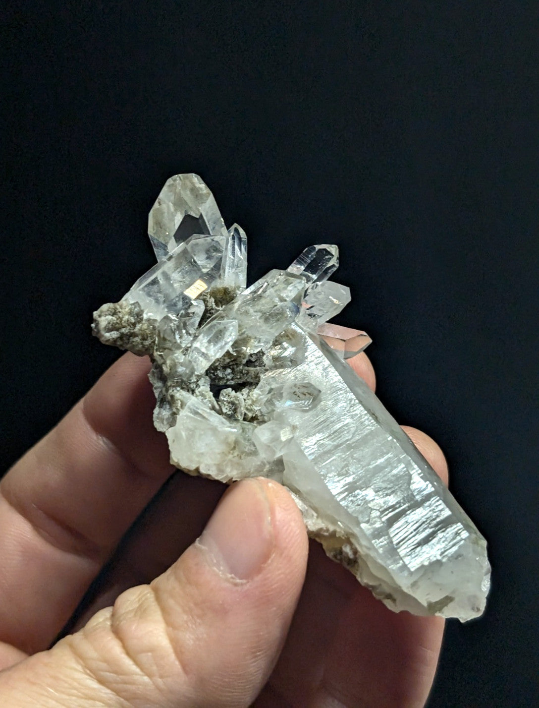 A translucent quartz crystal cluster with clear, faceted points and a rough, grayish matrix base.
