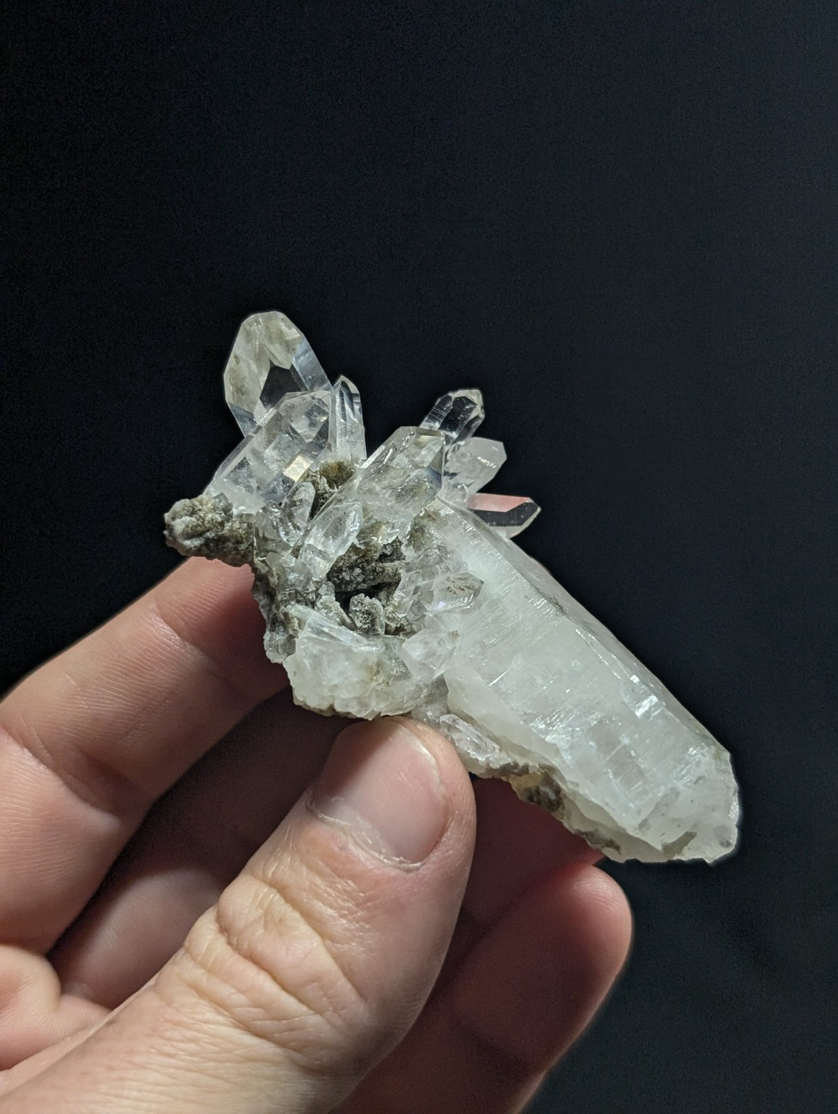 A translucent, clear quartz crystal cluster with sharp geometric facets and a few darker mineral inclusions.
