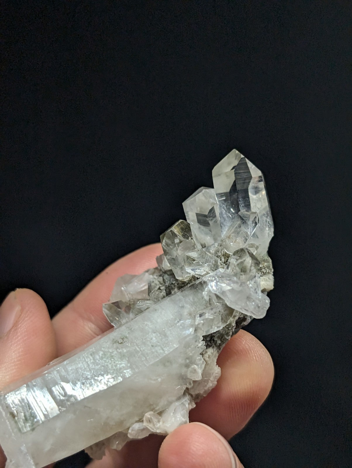 A translucent, clear quartz crystal cluster with sharp facets and a rougher base held in hand.