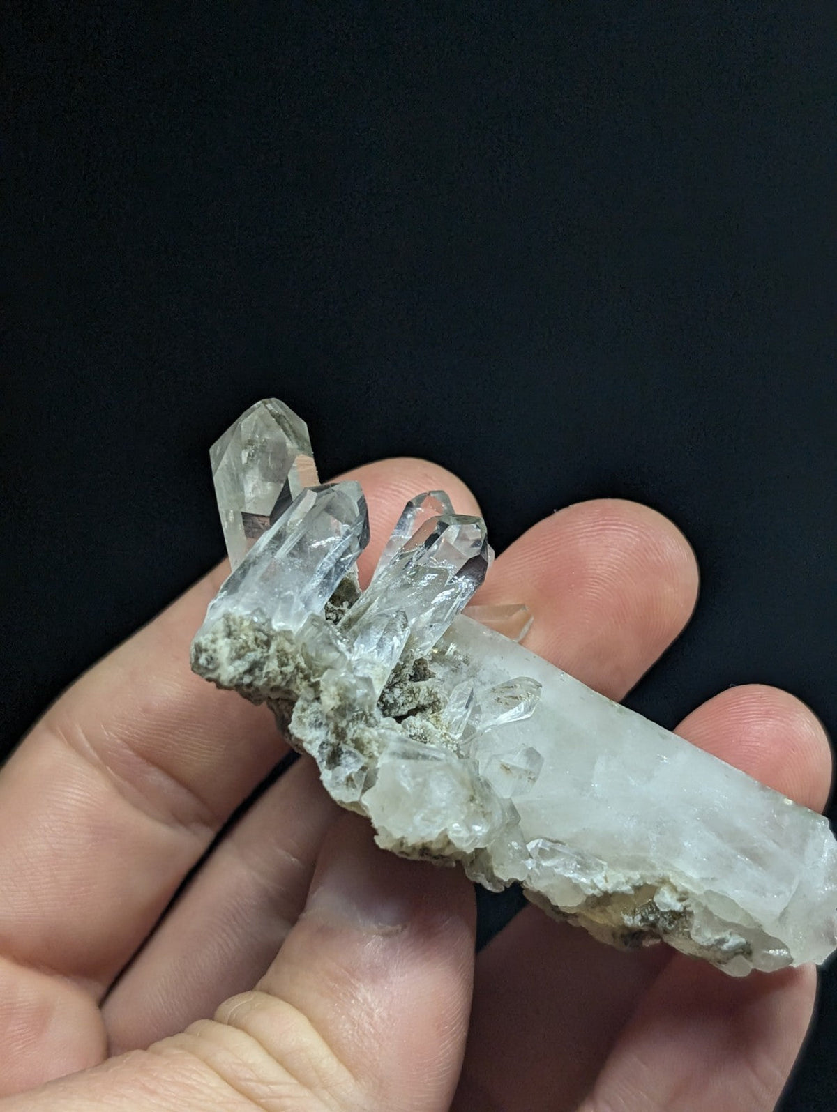 A translucent, clear quartz crystal cluster with sharp, pointed facets and a rough, earthy base.