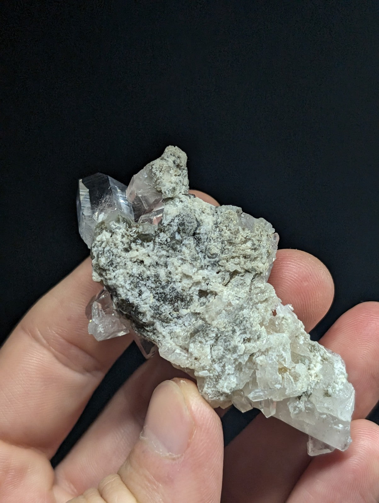 A translucent quartz crystal cluster with clear, faceted points emerging from a rough, grayish matrix.
