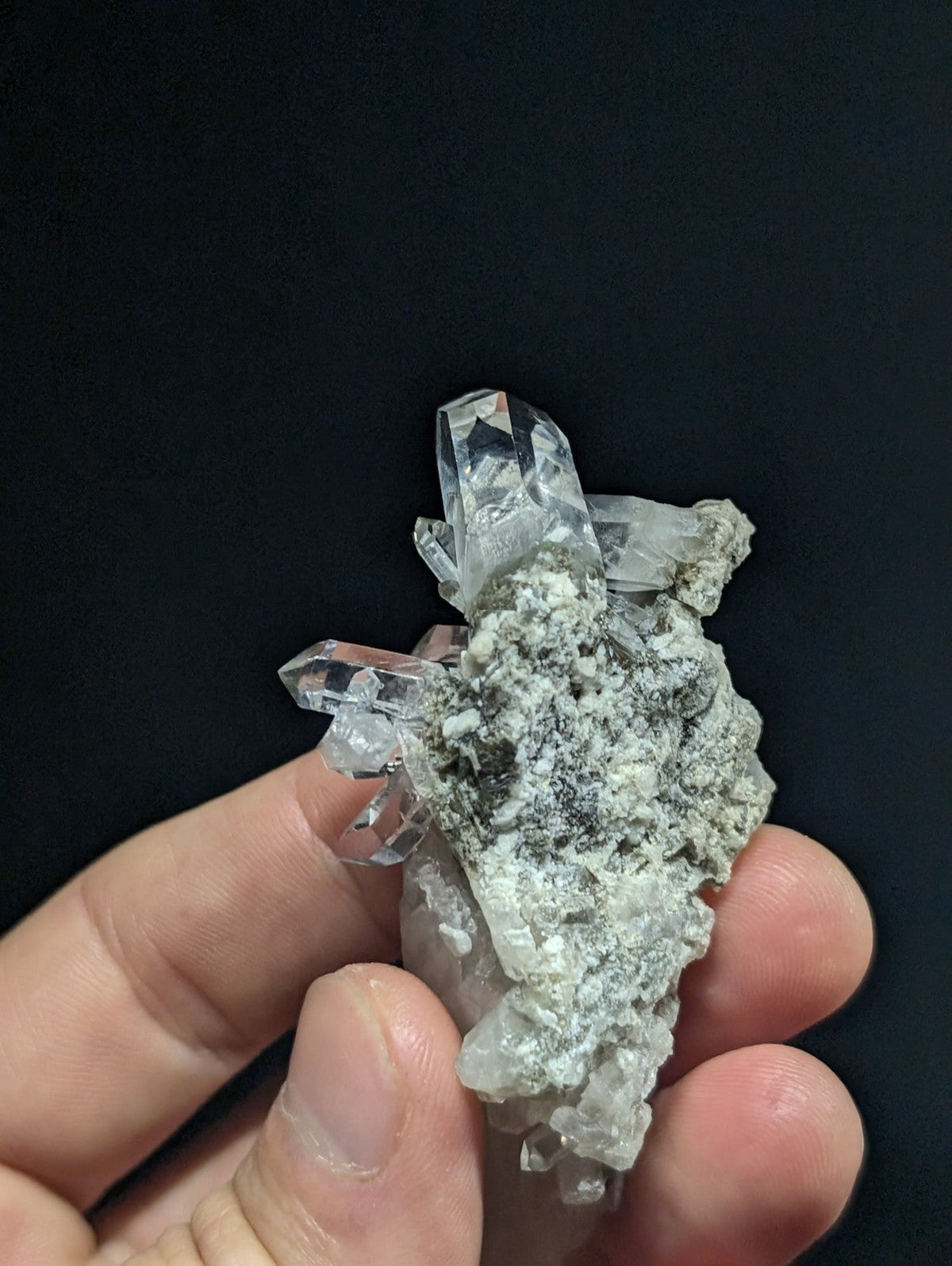 A cluster of clear, faceted quartz crystals growing from a grayish matrix.