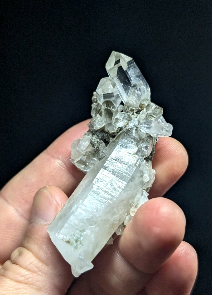 A translucent, clear quartz crystal cluster with a prominent elongated prismatic formation and smaller crystals growing from its base.
