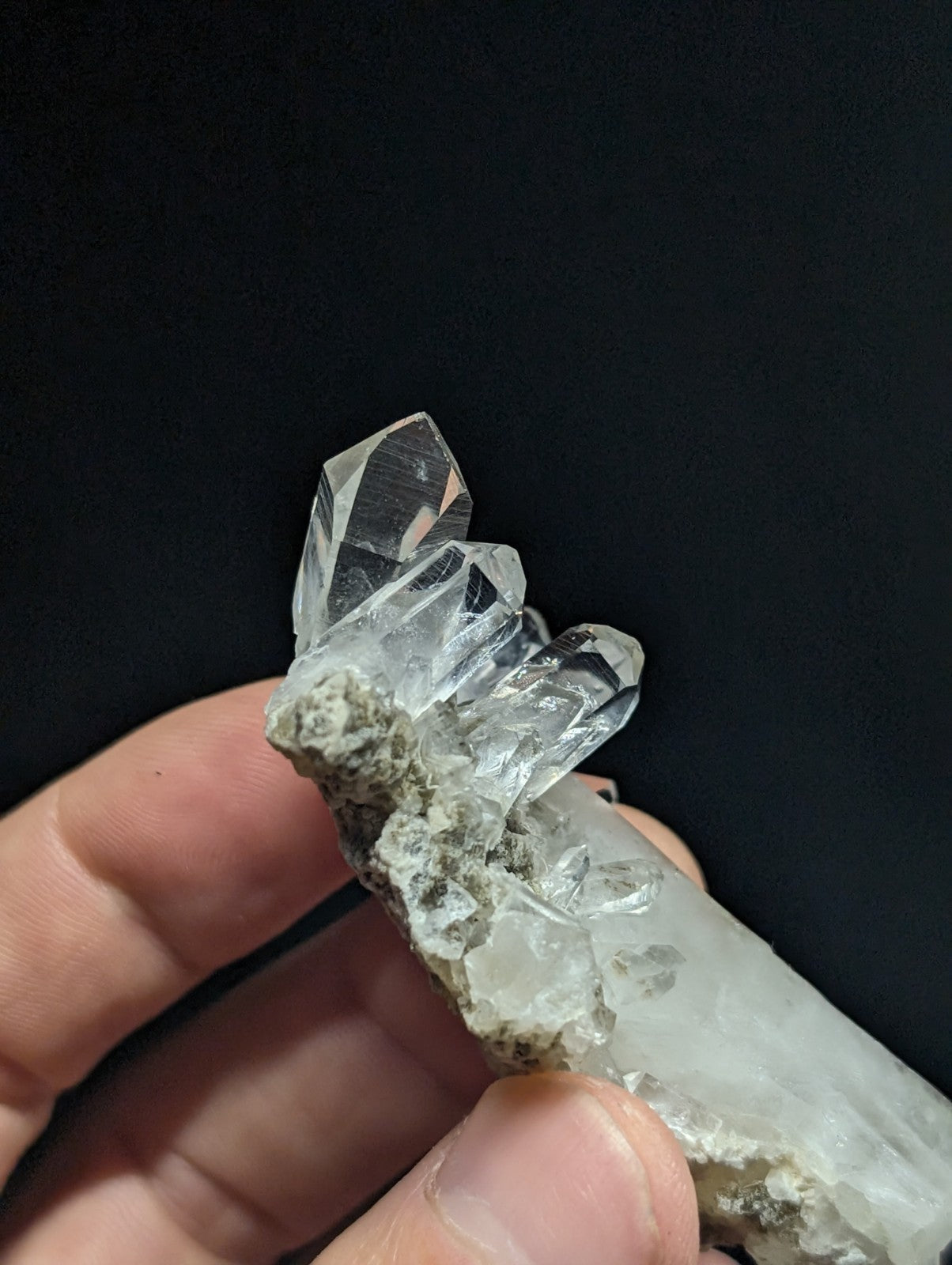 A clear quartz crystal cluster with sharp, faceted points emerging from a rough, grayish matrix.