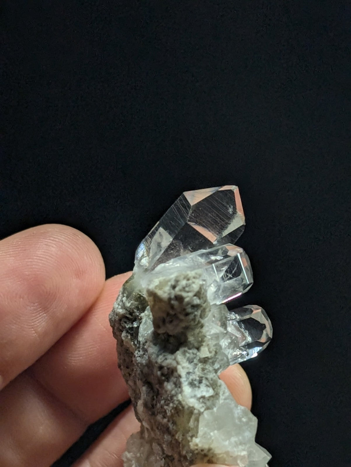 A clear quartz crystal cluster with sharp, faceted points emerging from a rough, grayish matrix.