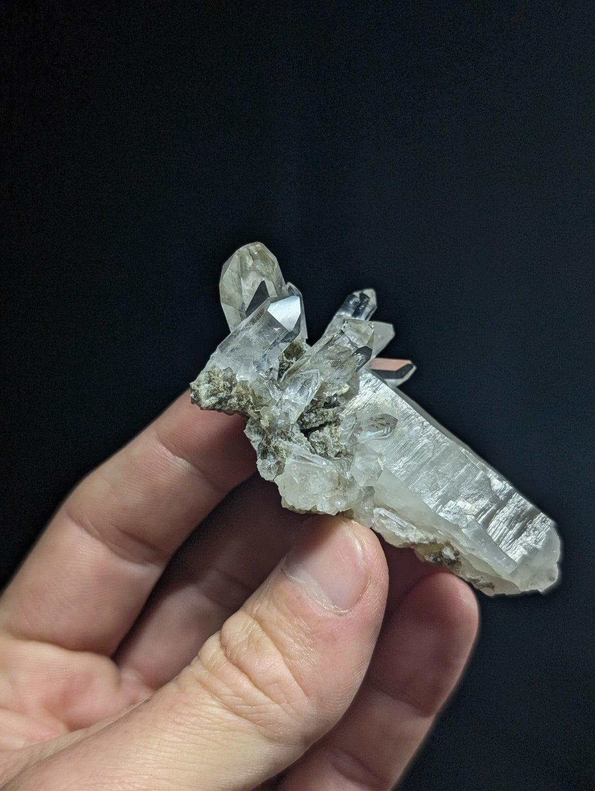 A translucent, clear quartz crystal cluster with a rough, earthy base and sharp, faceted points.