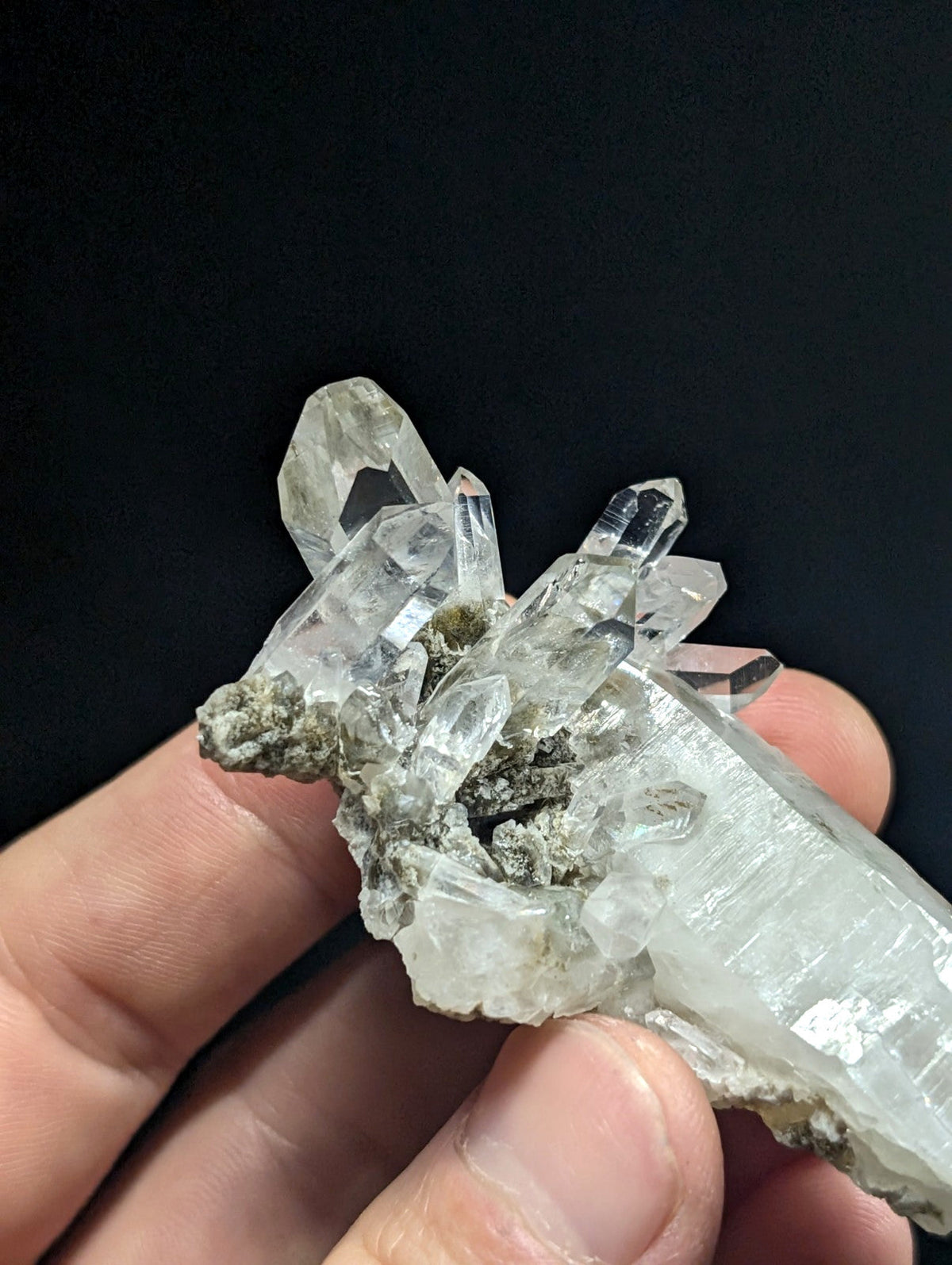 A cluster of clear, translucent quartz crystals with sharp facets and a few greenish-gray mineral inclusions.