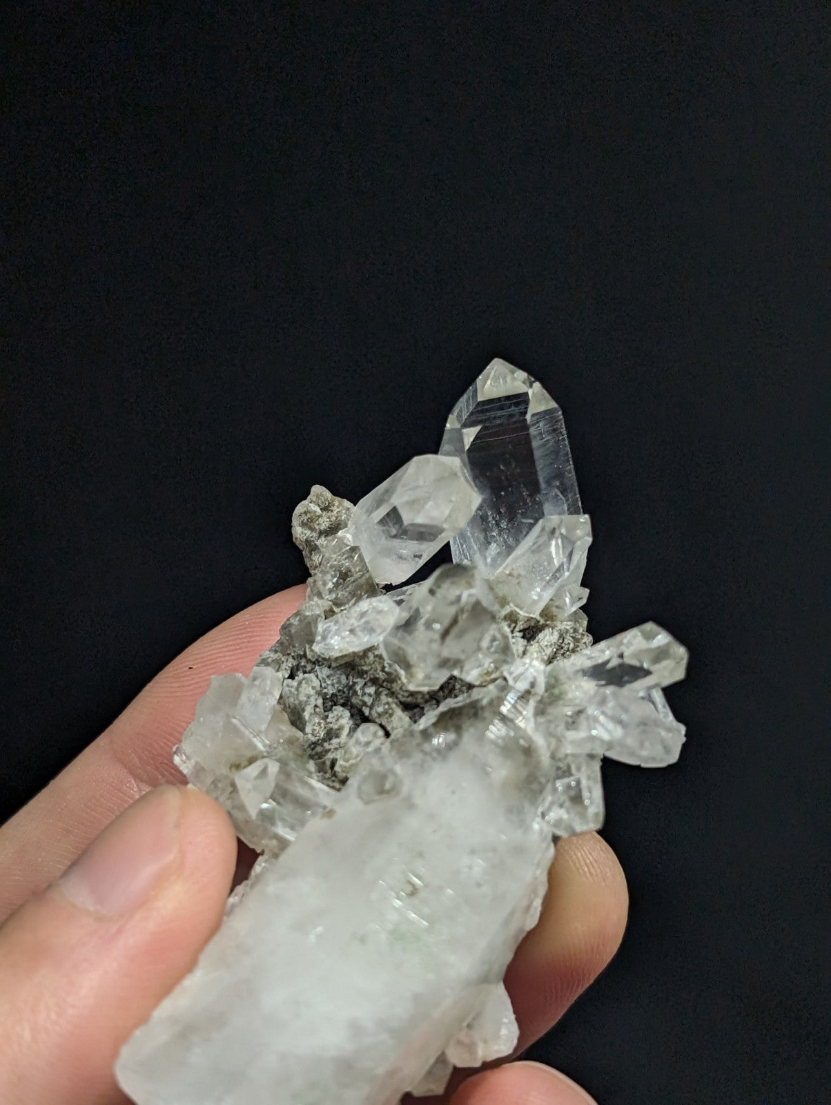 A cluster of clear, faceted quartz crystals with a grayish matrix base.