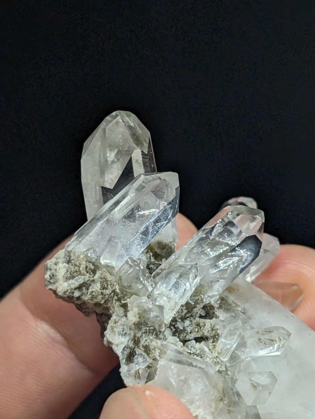 A cluster of clear, faceted quartz crystals growing from a grayish rock base.