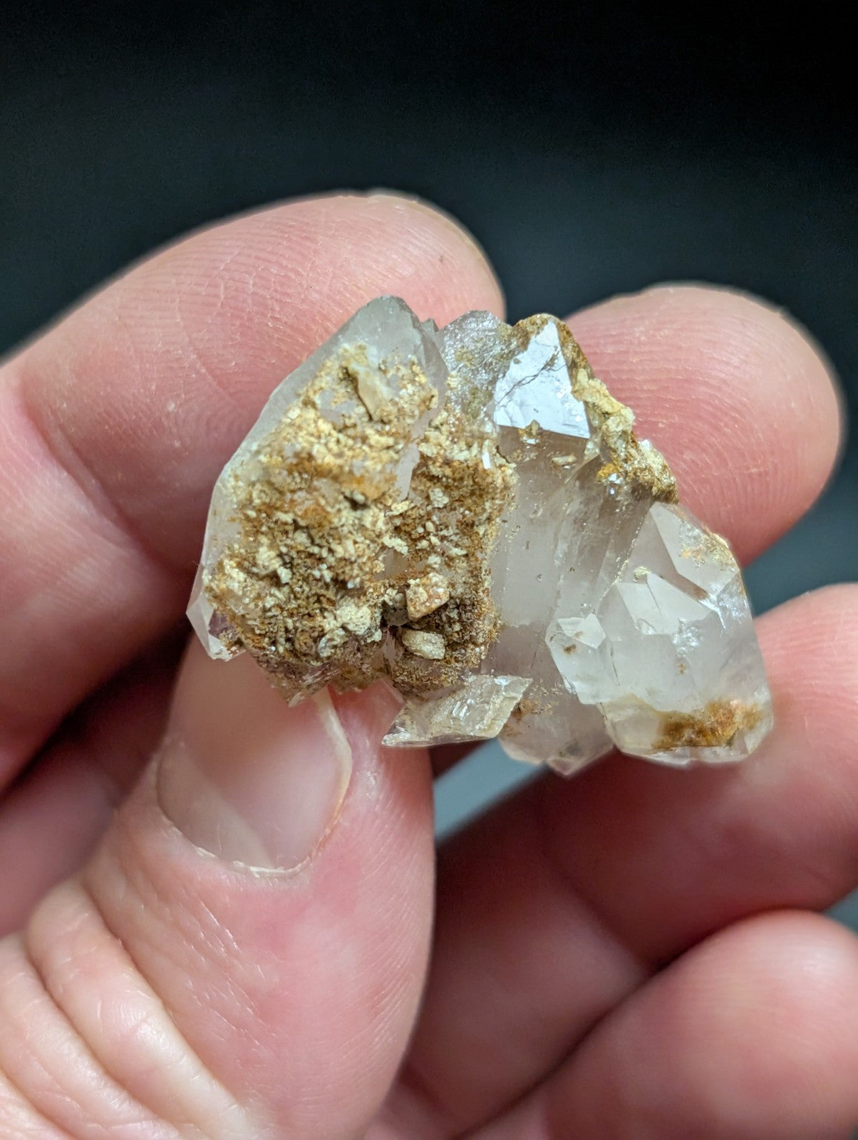 A translucent quartz crystal cluster with golden mineral inclusions, held gently between fingers.