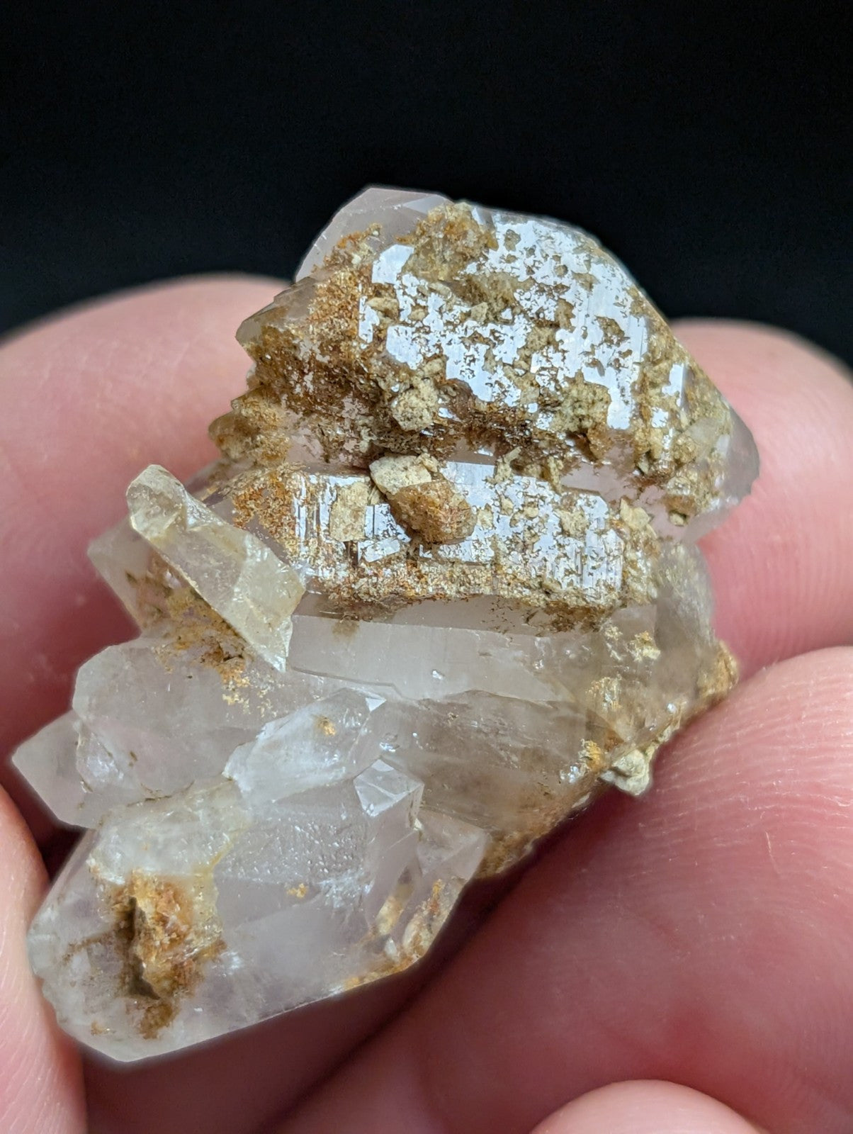 A translucent quartz crystal cluster with golden mineral inclusions, held gently between fingers.