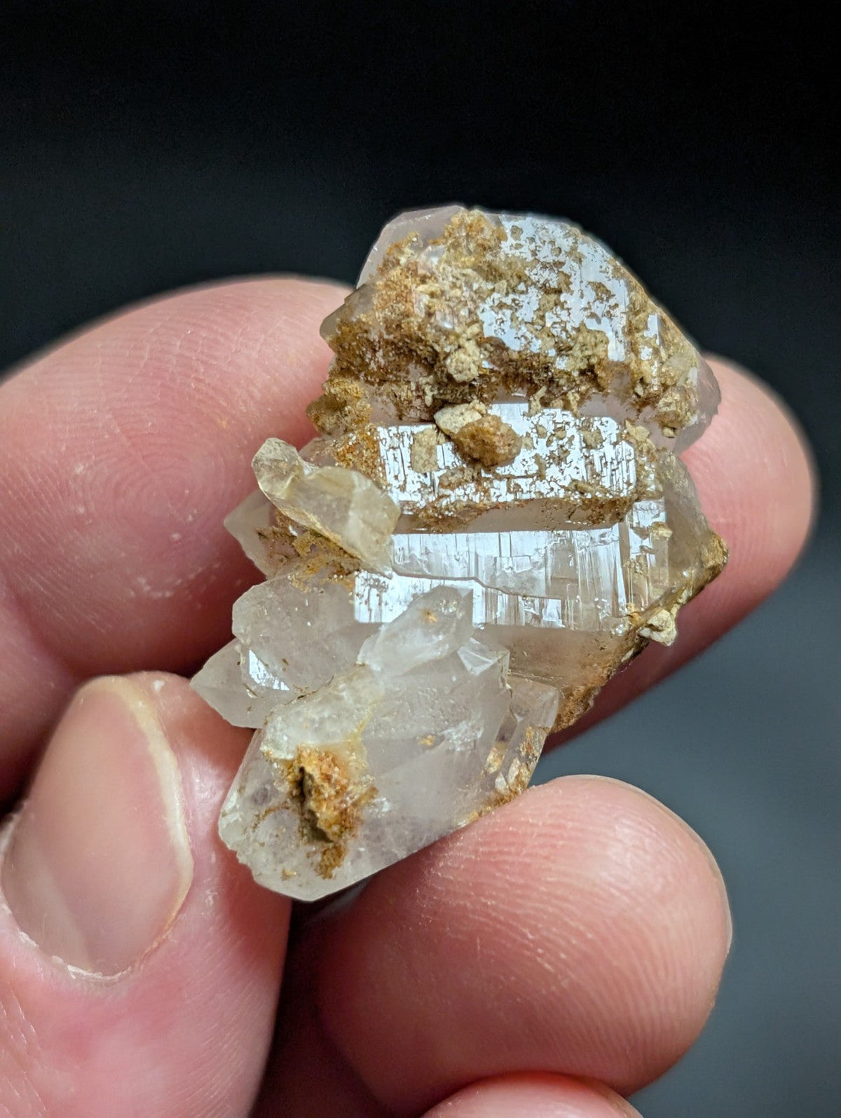 A translucent quartz crystal cluster with golden mineral inclusions, held gently between fingers.