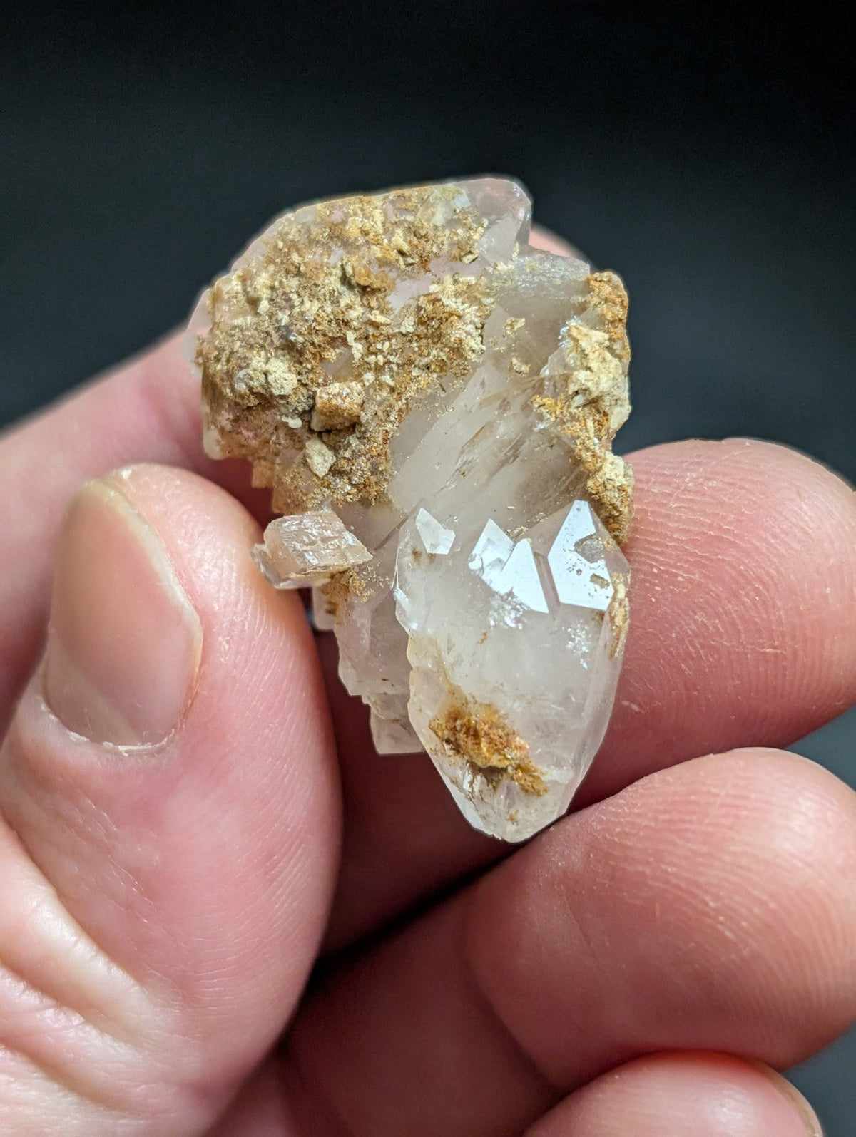 A translucent quartz crystal cluster with golden-brown mineral inclusions, held gently between fingers.