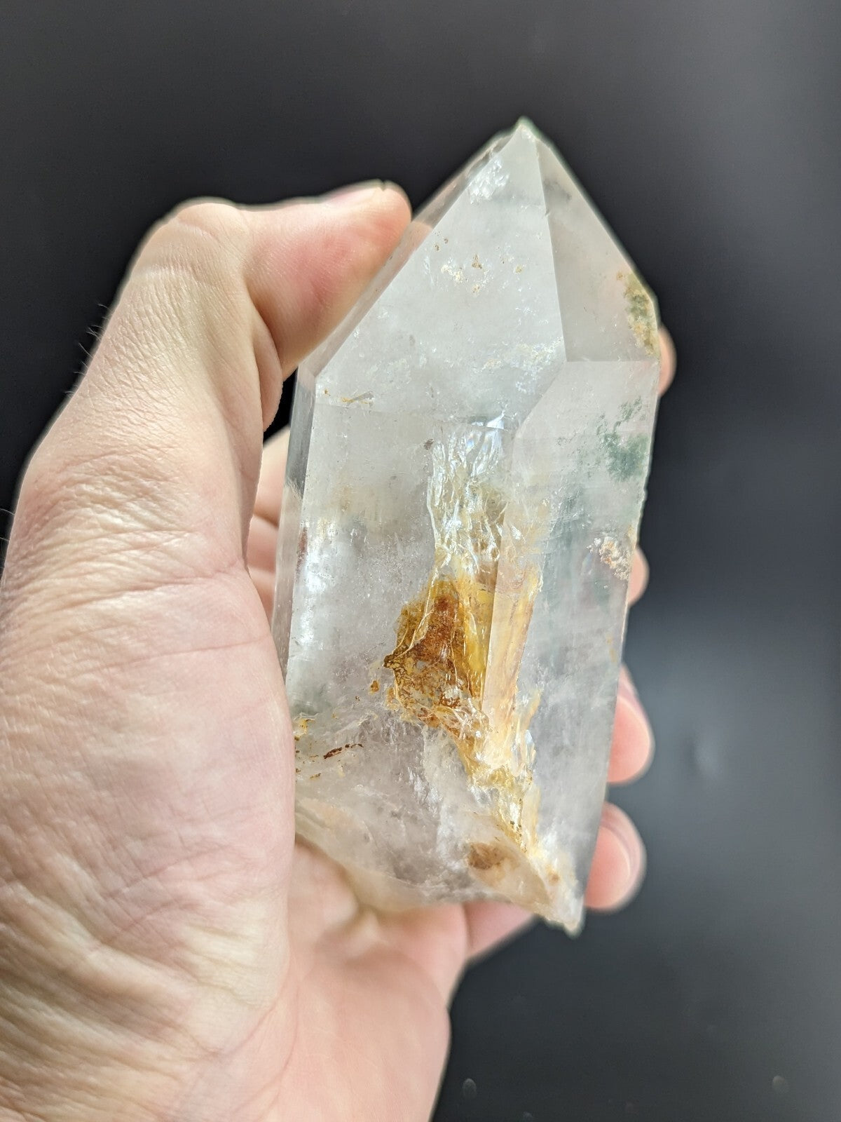 A translucent, clear quartz crystal with a natural golden inclusion and subtle greenish veining.