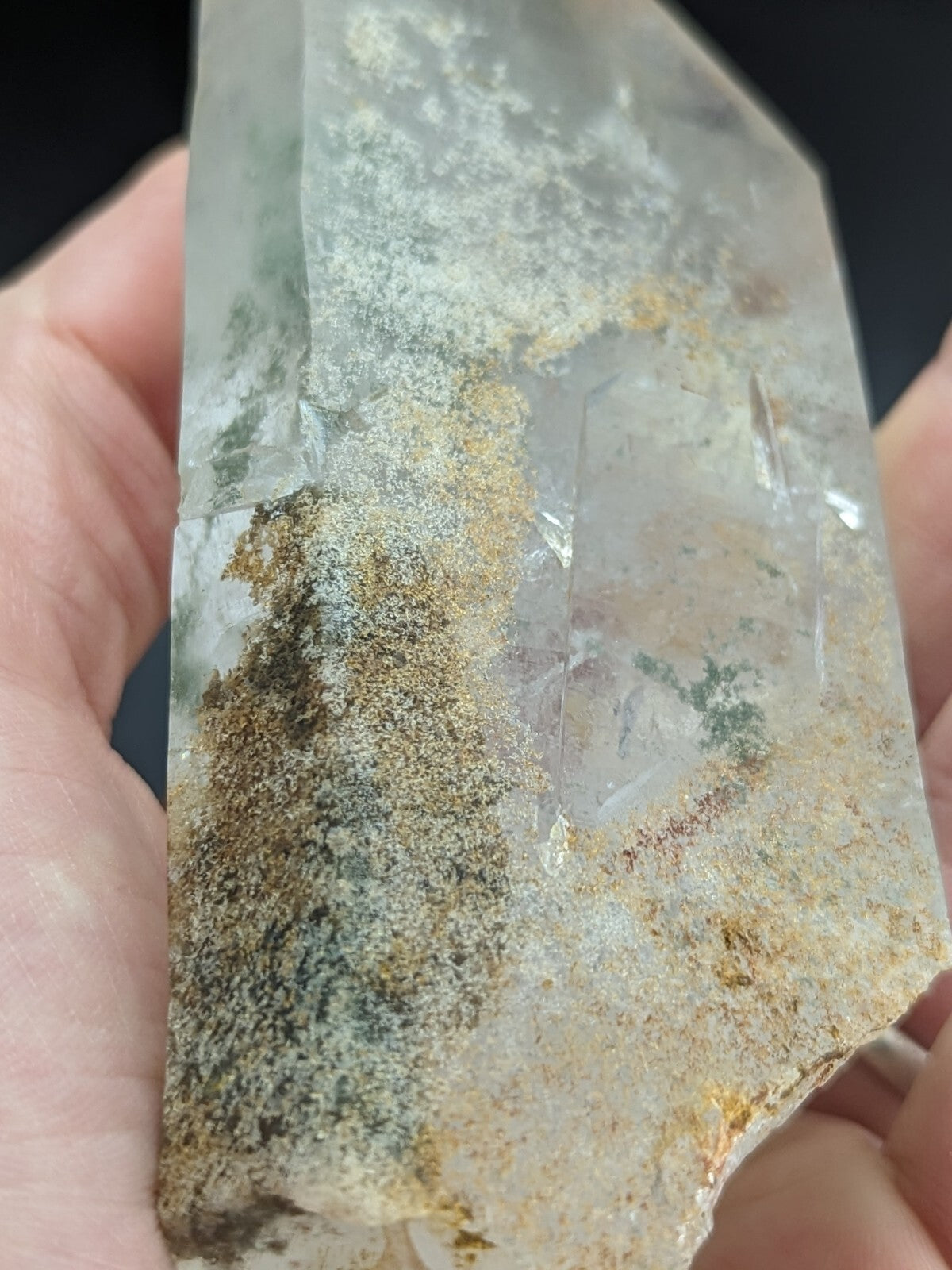 A translucent quartz crystal with natural inclusions and earthy mineral streaks, held gently between fingers.