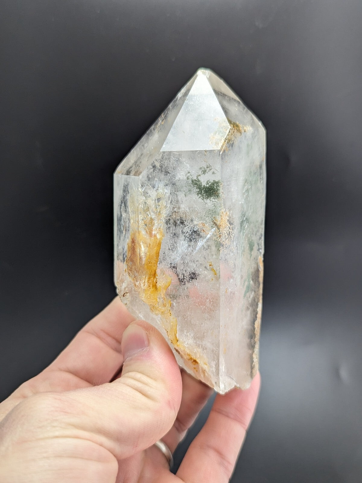 A translucent, clear quartz crystal with natural inclusions of golden and greenish hues.