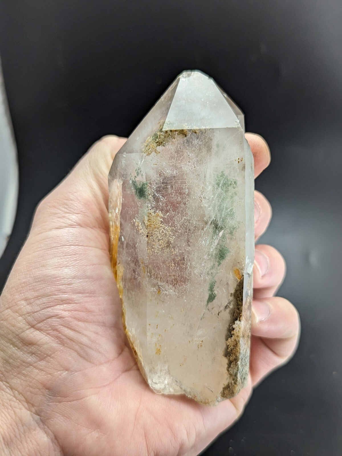 A translucent, clear quartz crystal with natural green and yellow inclusions held gently in a hand.
