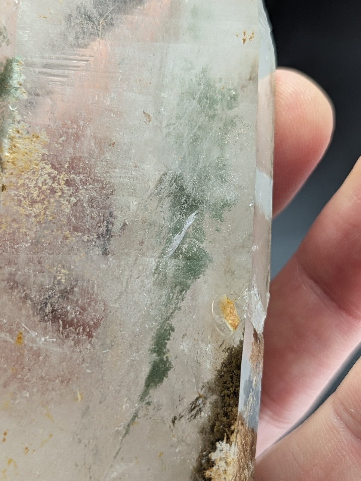 A translucent quartz crystal with natural green and golden inclusions, held gently by a hand.